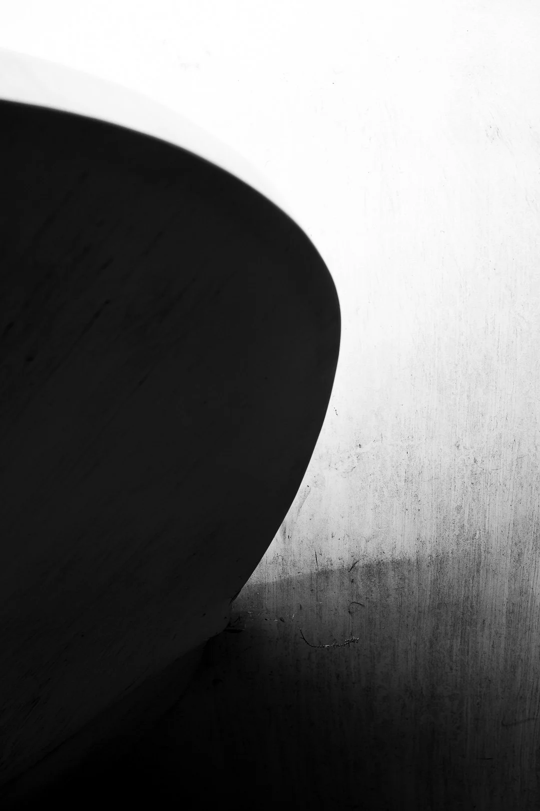 Close-up black and white photo of a curved, dark object with a smooth surface, positioned on a textured, light-colored background.
