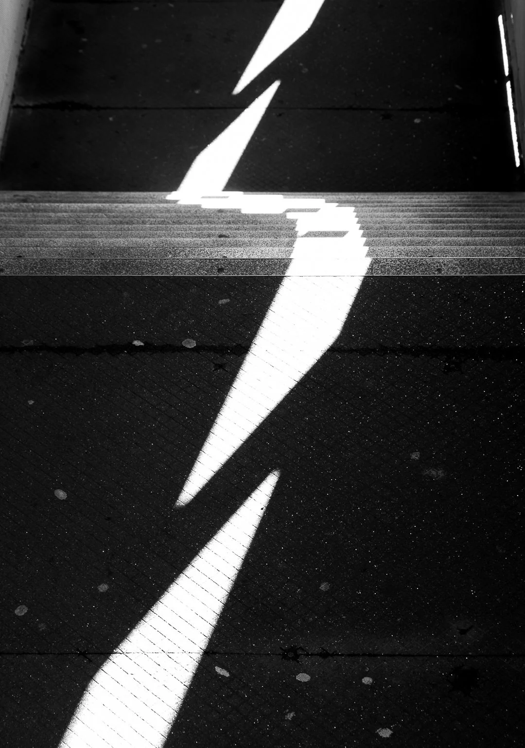 A black and white image of a stairway with a lightning bolt pattern on the risers, reflected on a shiny black surface.