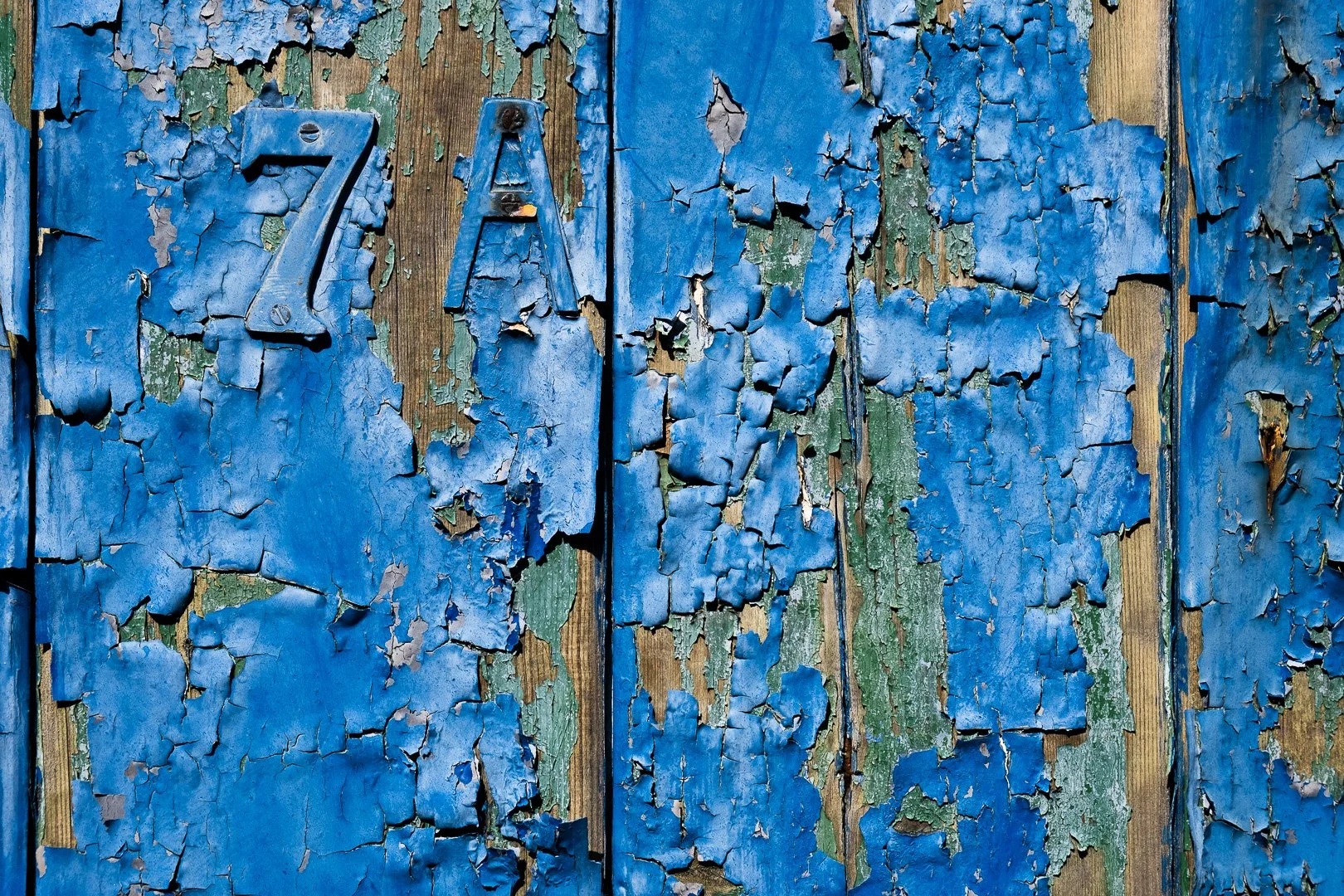 Close-up of weathered blue painted wooden surface with peeling paint and faded 'ZAP' letters.