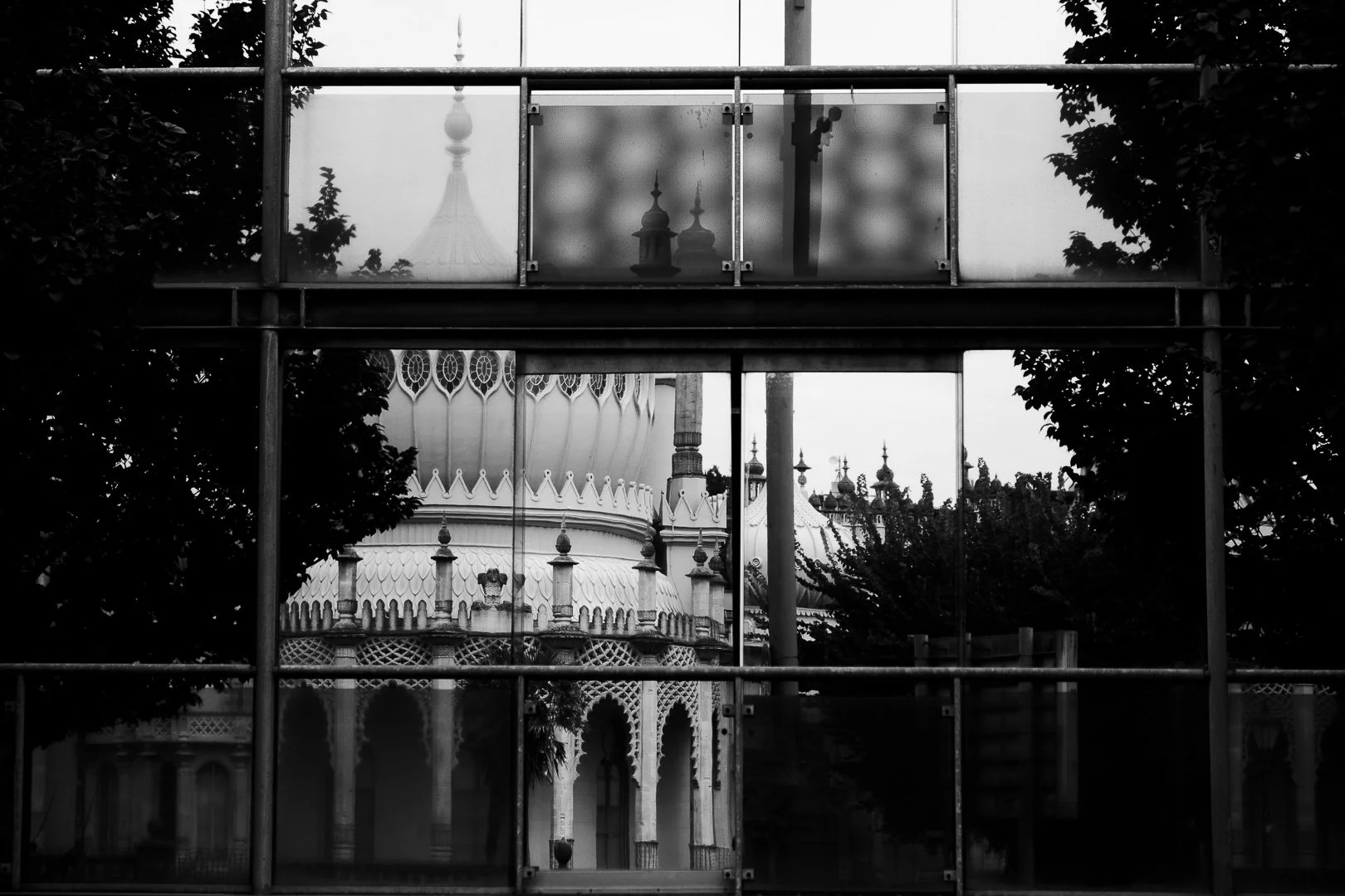 Black and white photo of the Taj Mahal framed by a glass and metal structure with trees on either side.