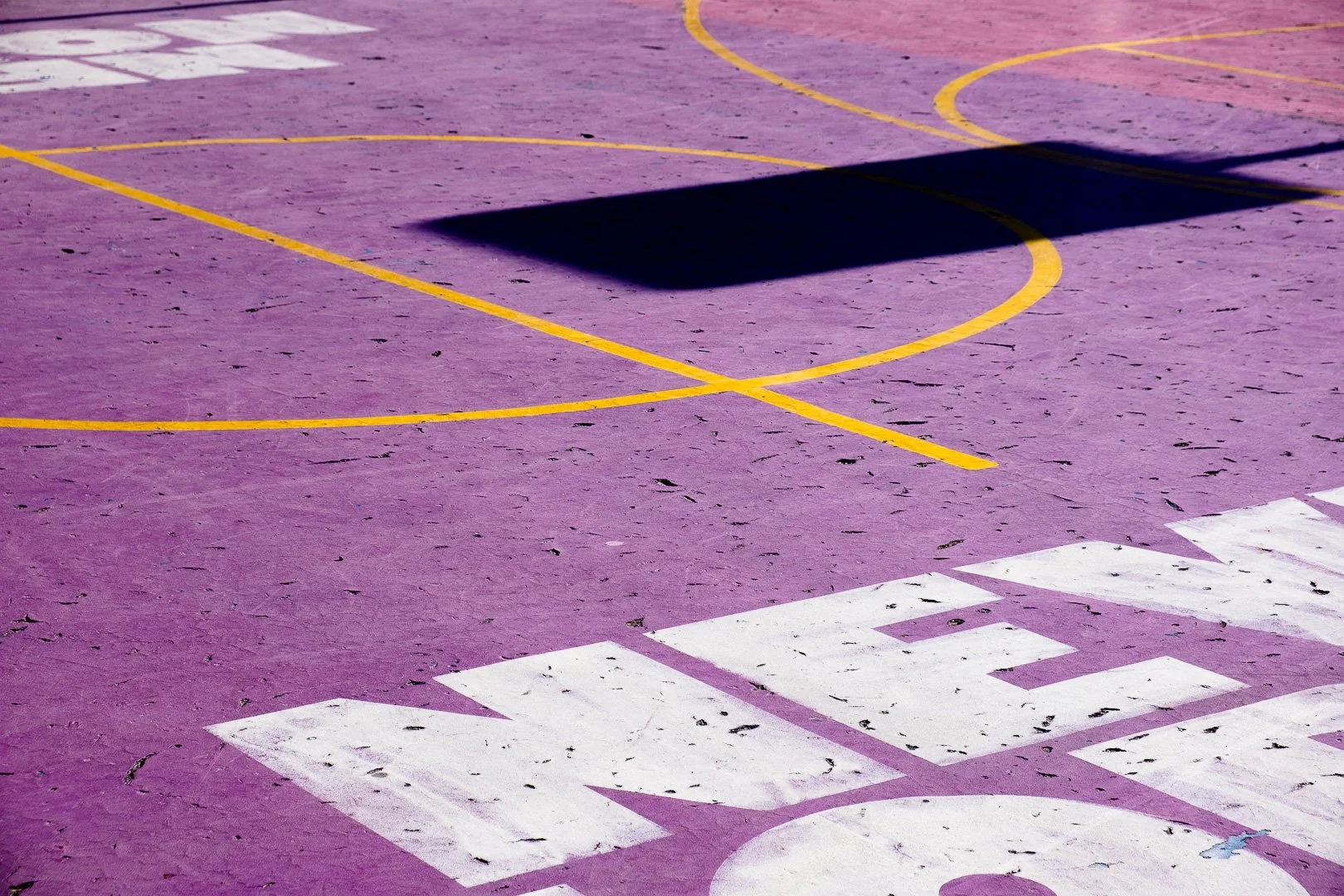 A close-up view of a purple basketball court with yellow court lines and the word 'SCHOOL' painted in white near the edge.