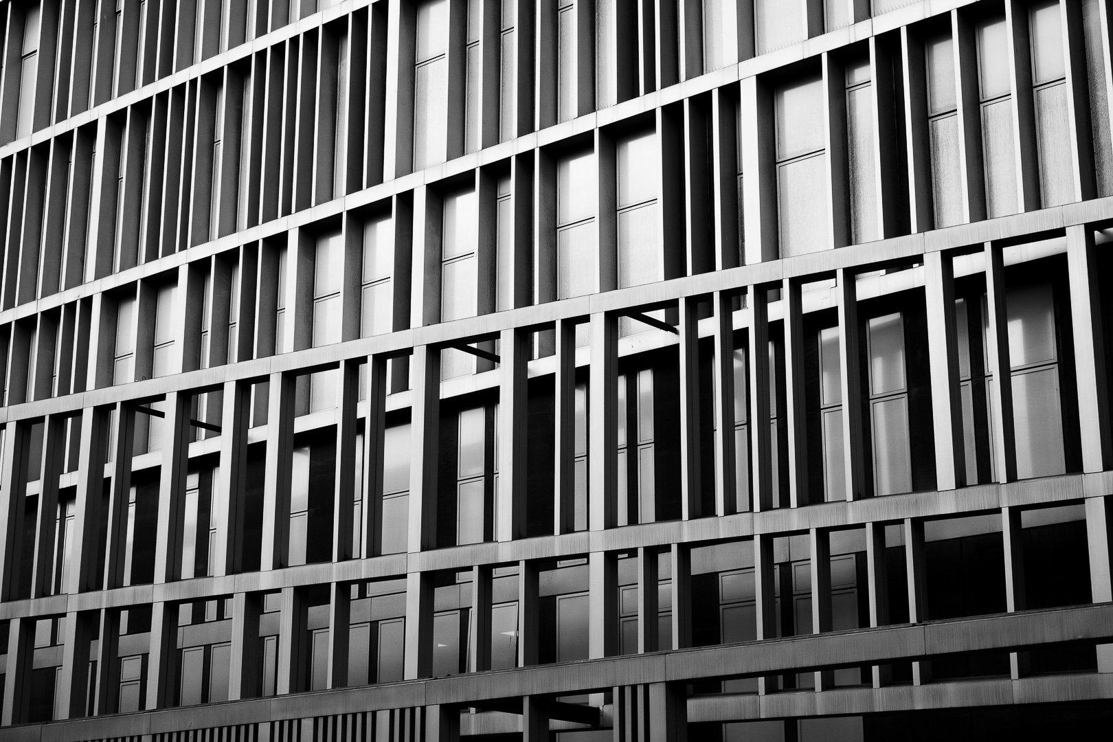 Modern multi-story building with a facade featuring vertical and horizontal metal beams and large windows, black and white photo.