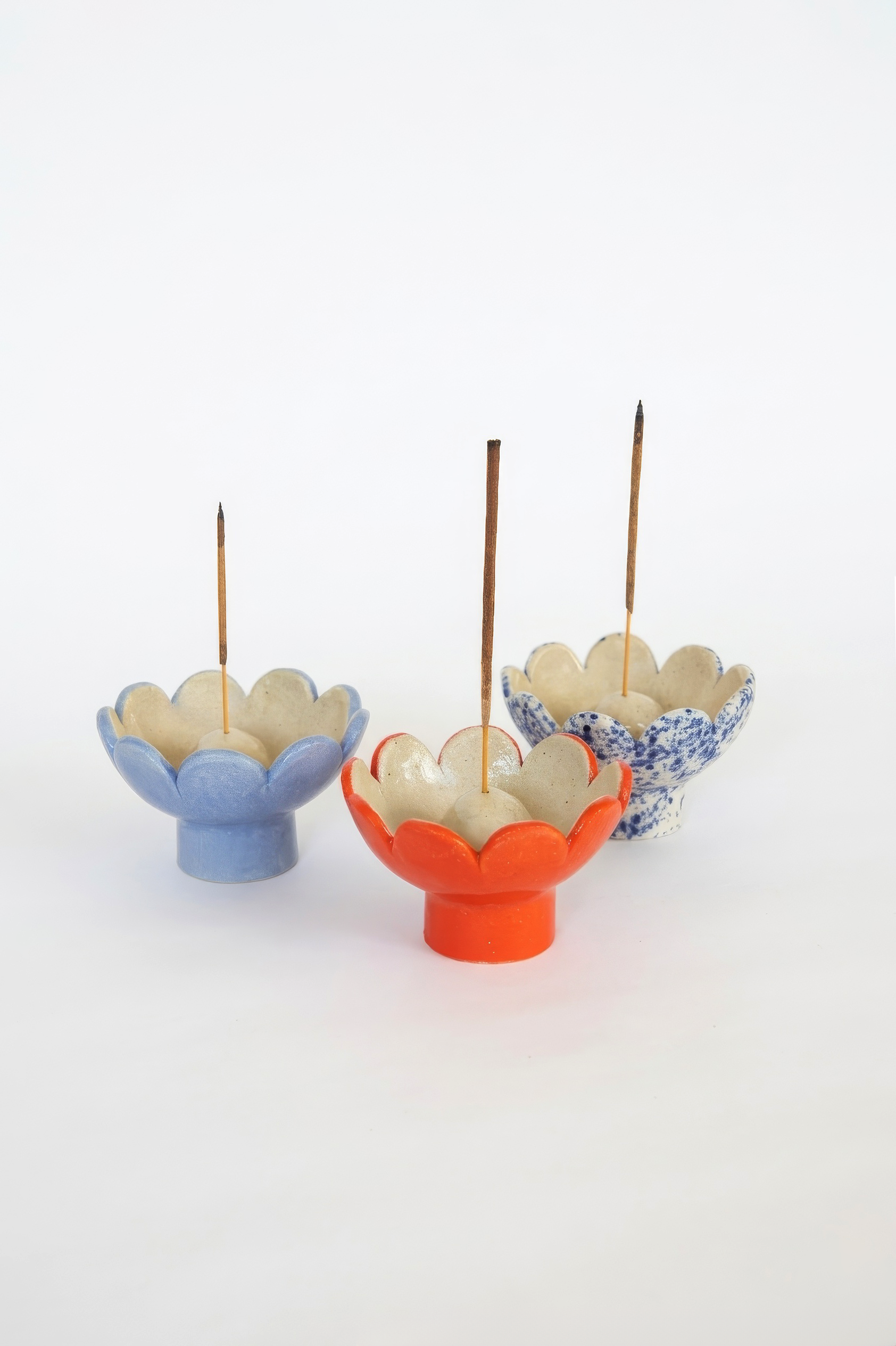 Three colorful ceramic flower-shaped incense holders with upright incense sticks on a white background