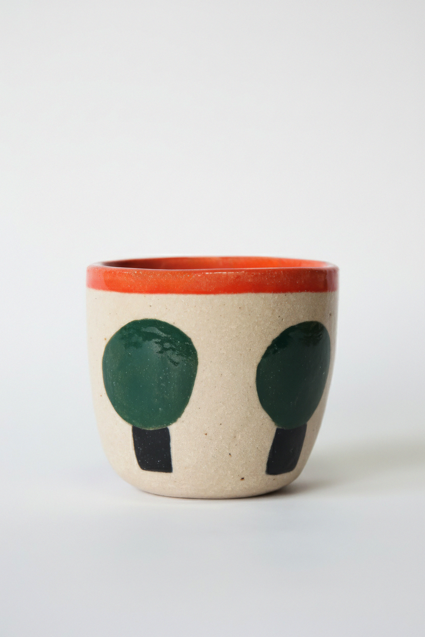 Handcrafted ceramic mug with a red rim and abstract green and black face design