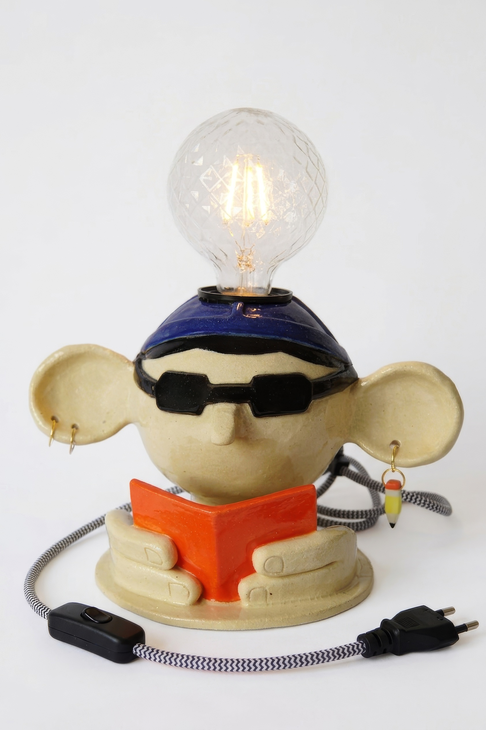 Handmade ceramic character table lamp with large ears, black sunglasses, orange bow tie, glowing textured light bulb, and patterned power cord