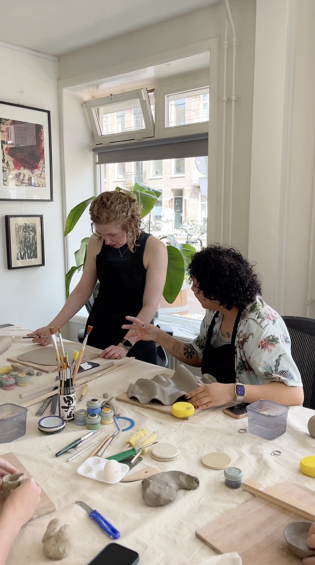 Two people work with clay and paintbrushes during a pottery workshop at a craft table.