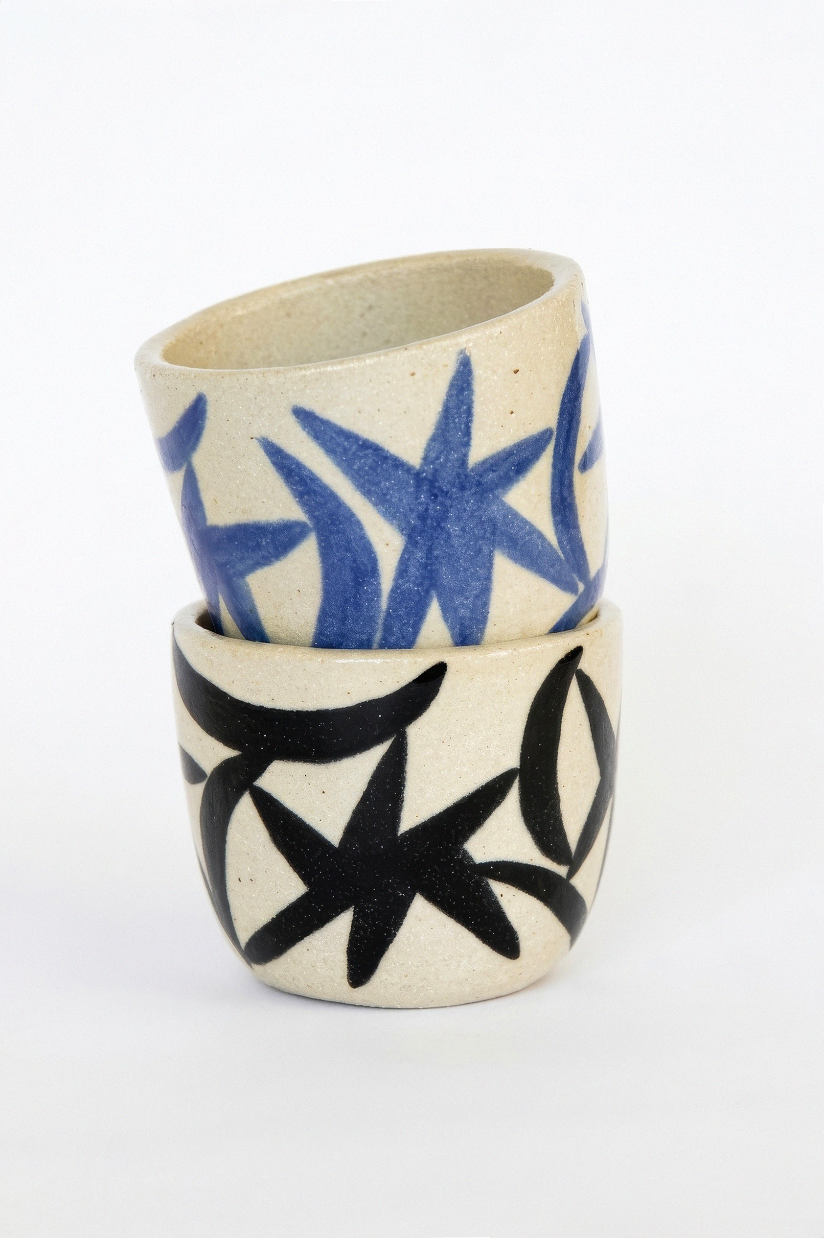 Two stacked ceramic cups with abstract black and blue starburst patterns on a cream background