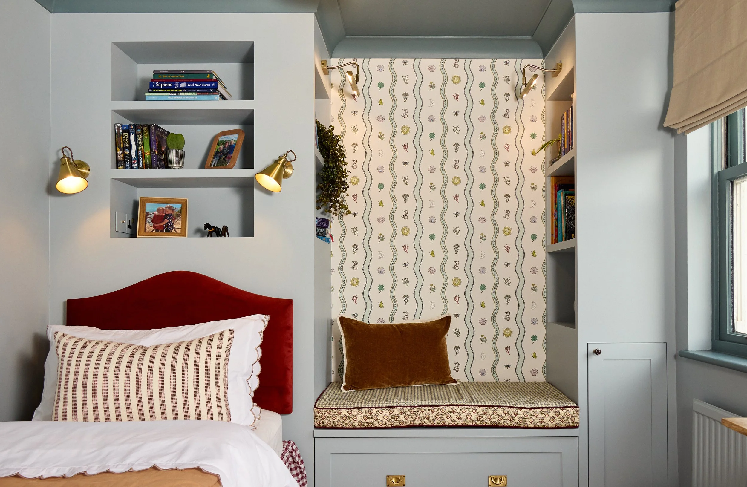 children room in light blue muted tones. with burgundy accents and wave patterns. mid shot of bed and reading nook