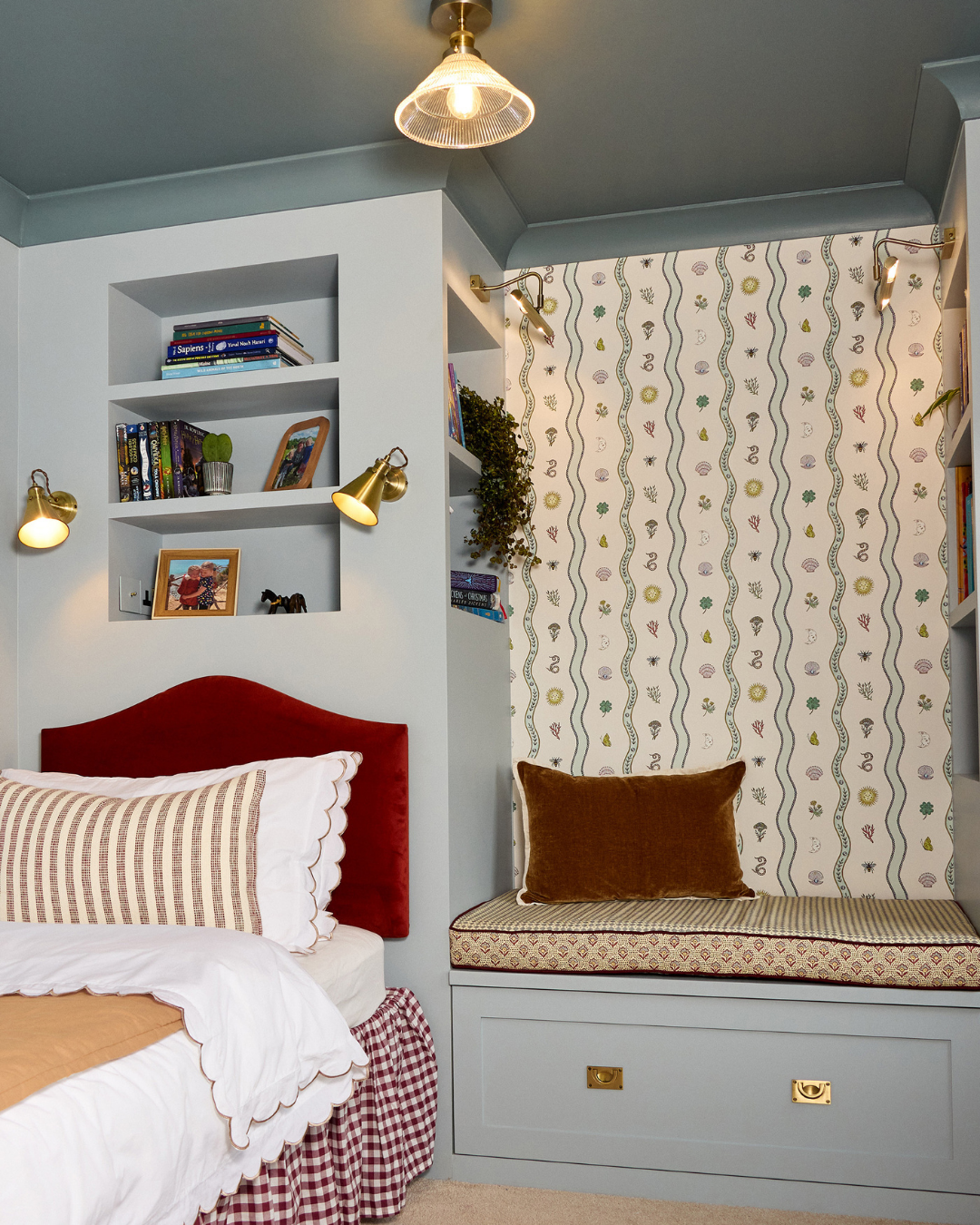 children room in light blue muted tones. with burgundy accents and wave patterns. side shot of bed and reading nook
