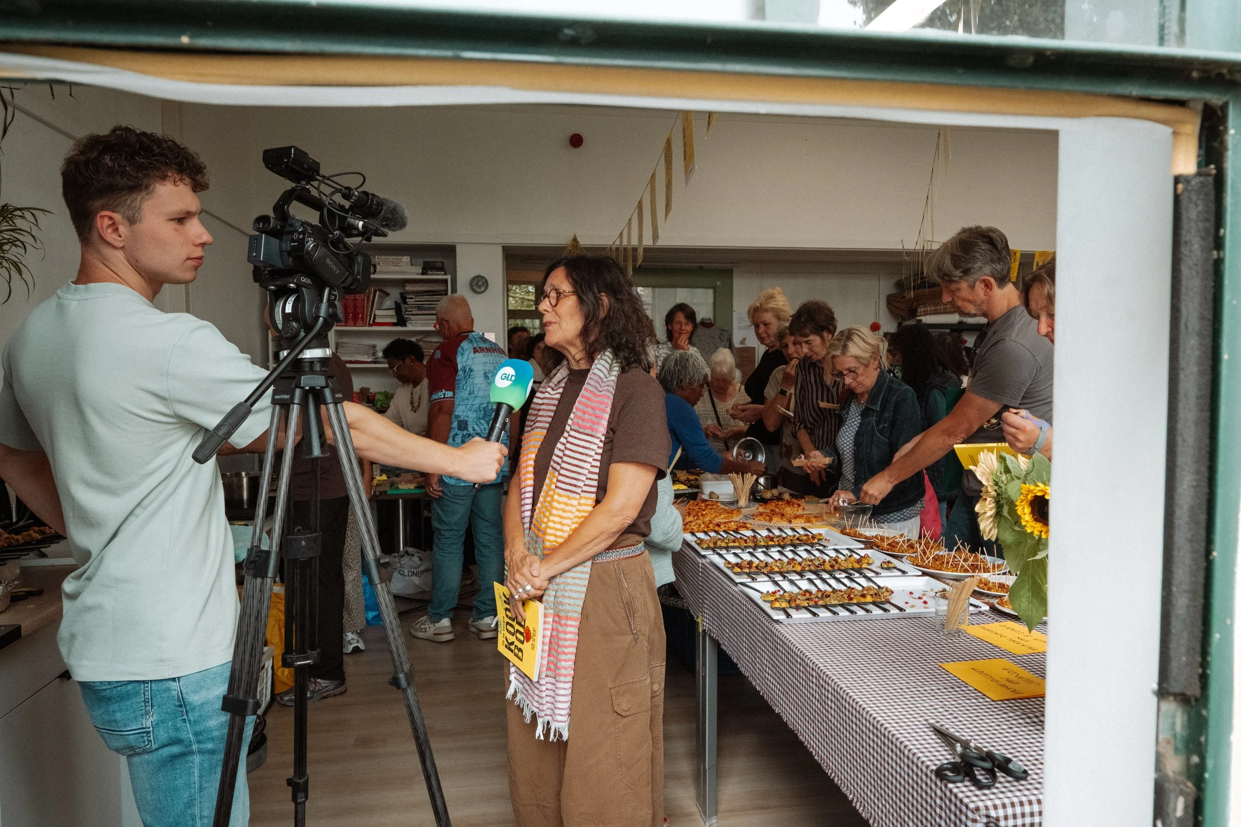 Interview met een vrouw bij een markt met hapjes en bloemen.