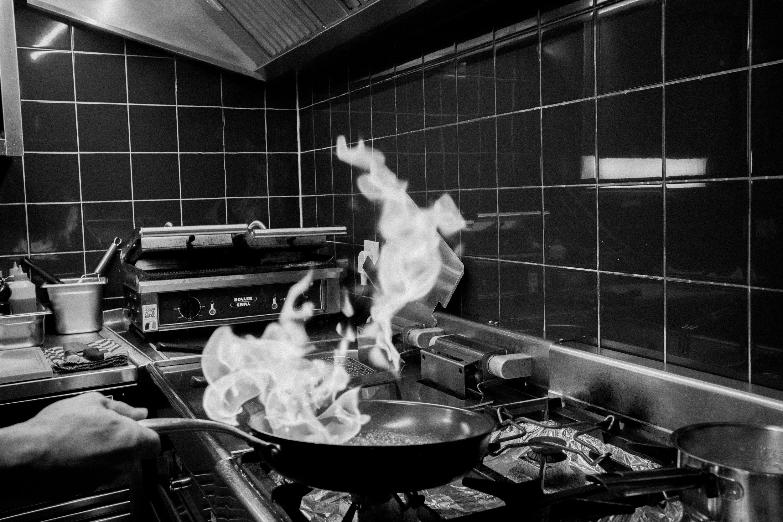 Een professionele keuken met een fornuis dat in brand staat en een chef-kok die een gerecht kookt.