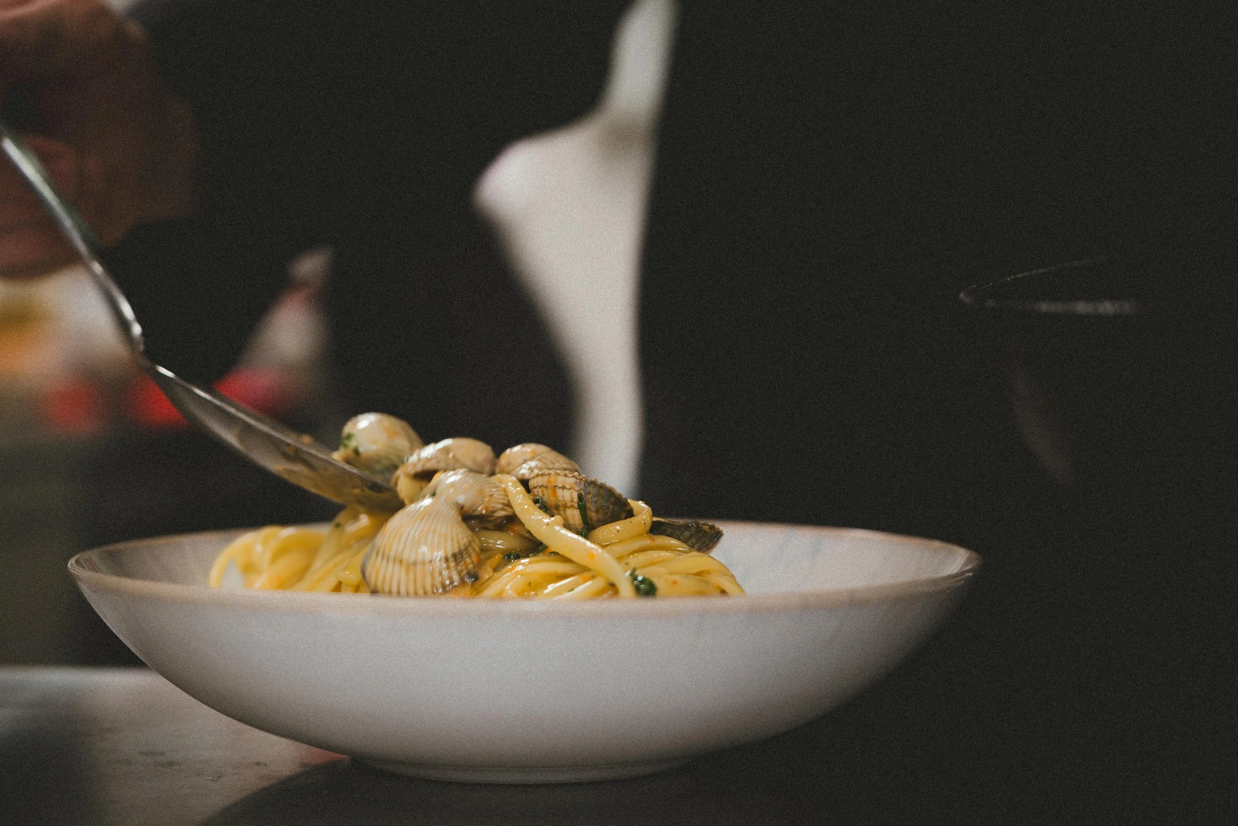 Bord met pasta en schelpdieren, met een persoon die saus of olie over de pasta schenkt.