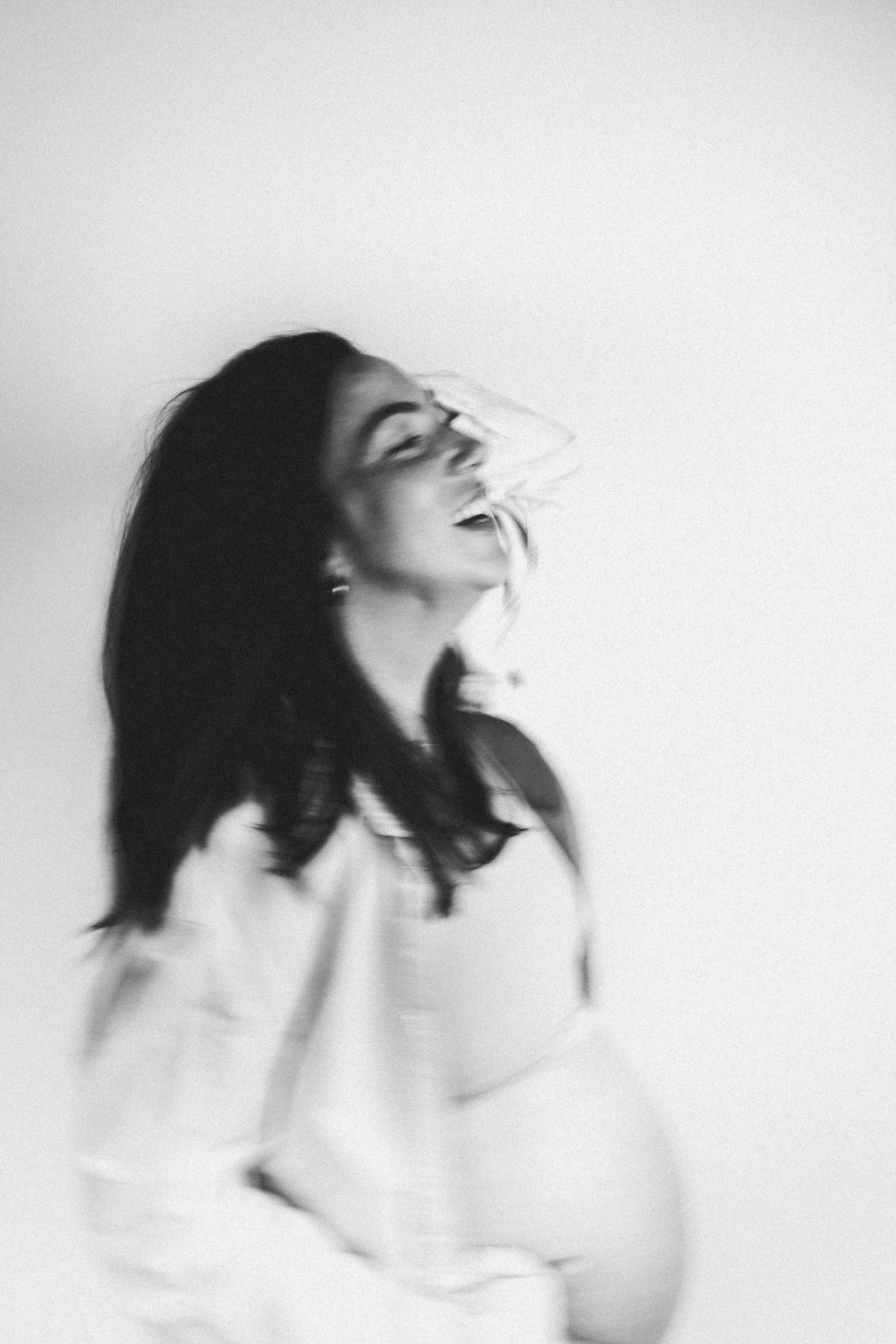 Zwart-wit foto van lachende vrouw met lang haar die haar hoofd naar achteren kantelt. zwanger zwangerschap buik baby vogue blurry effect