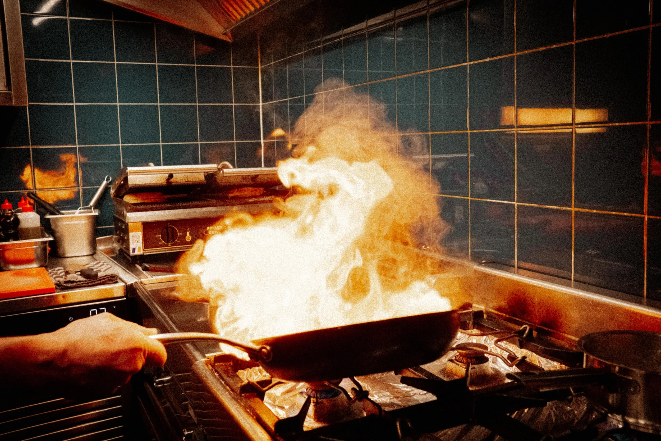 Een keuken met een fornuis waarop een pan staat die vlammen uitstoot, terwijl er een vuurspuwend fenomeen plaatsvindt.