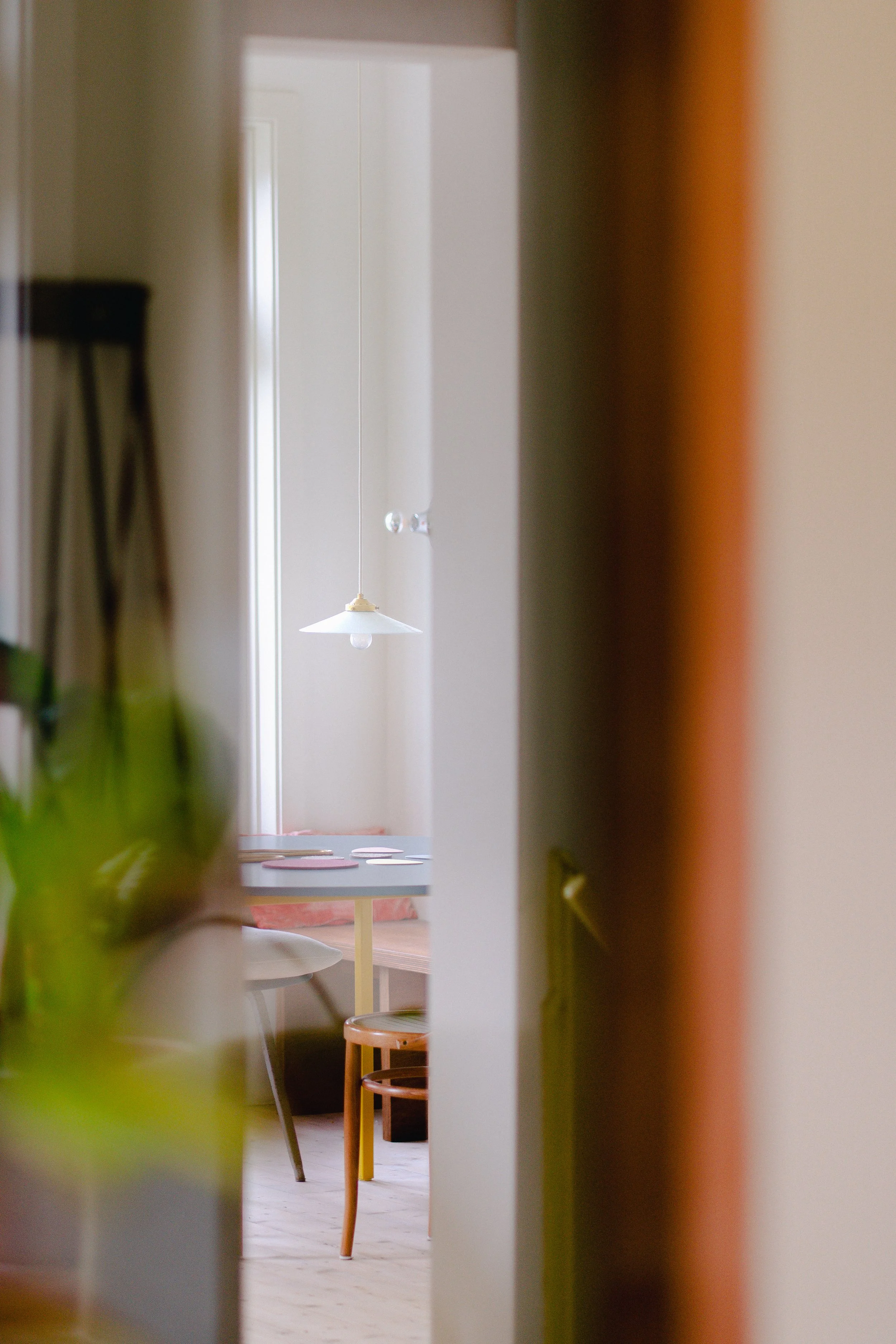 Binnenzitkamer met eettafel en stoelen, witte hanglamp, houten vloer, afgezien door een deur of tussenwand.