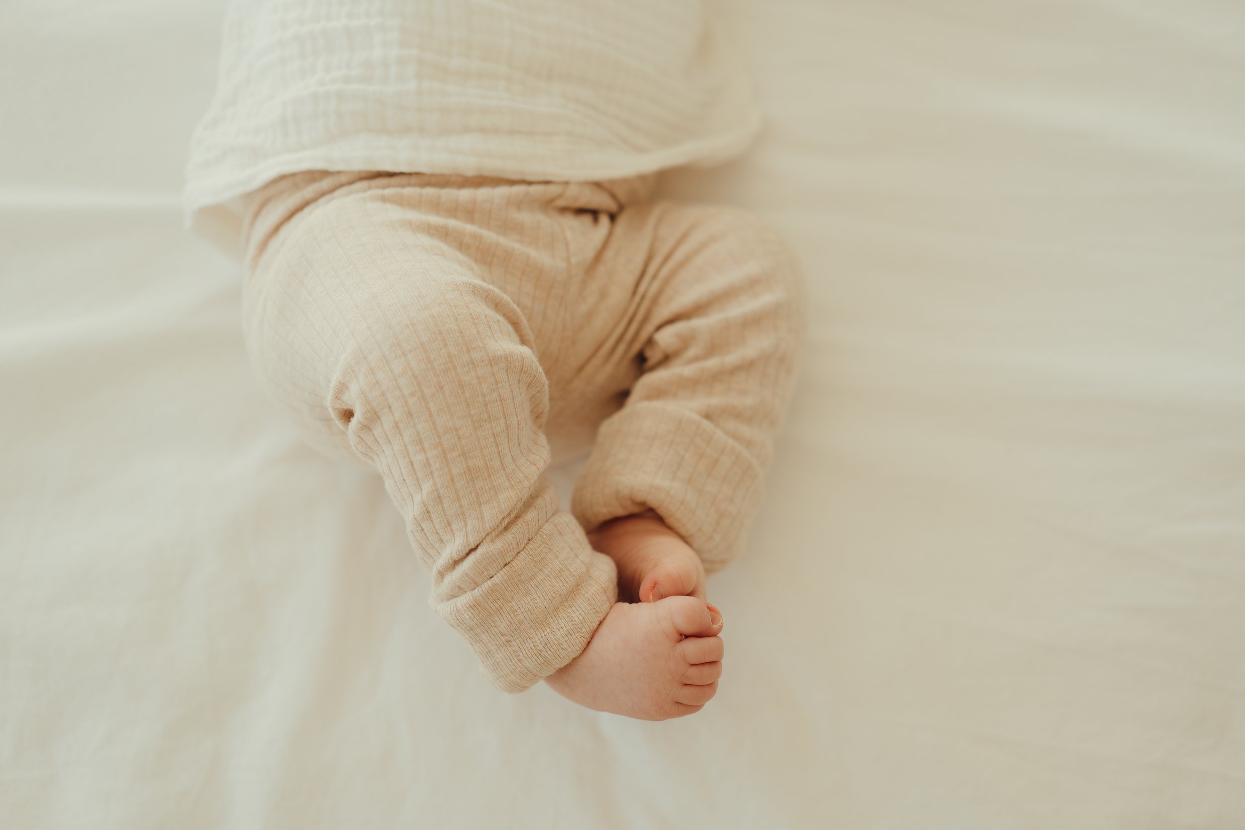 Close-up van een baby met een beige trui, met gesloten vuisten en knuistje stevig vastzittend.