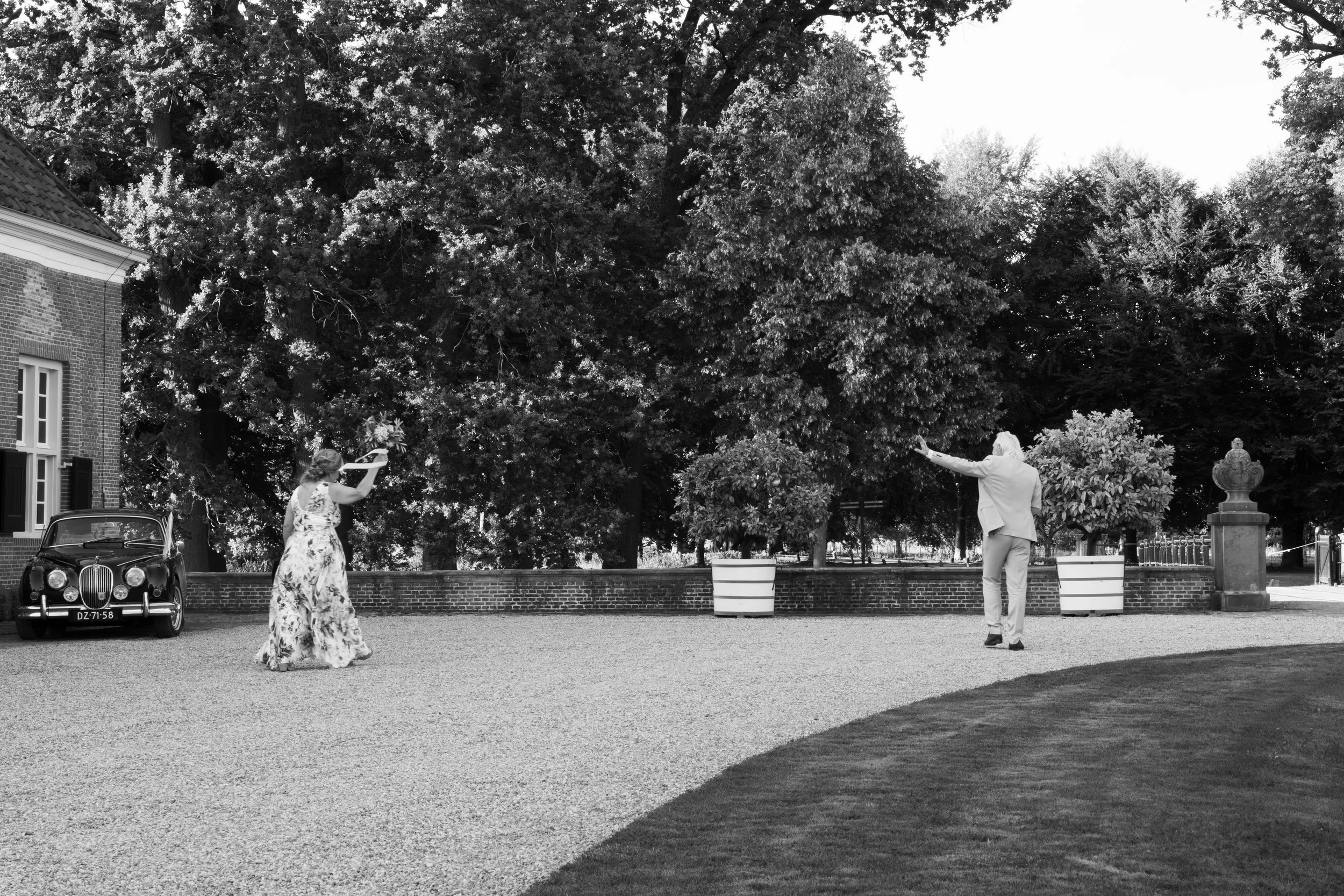 Een zwart-witfoto van een tuinfeest met een man en een vrouw die dansen, omringd door grote bomen en historische gebouwen.