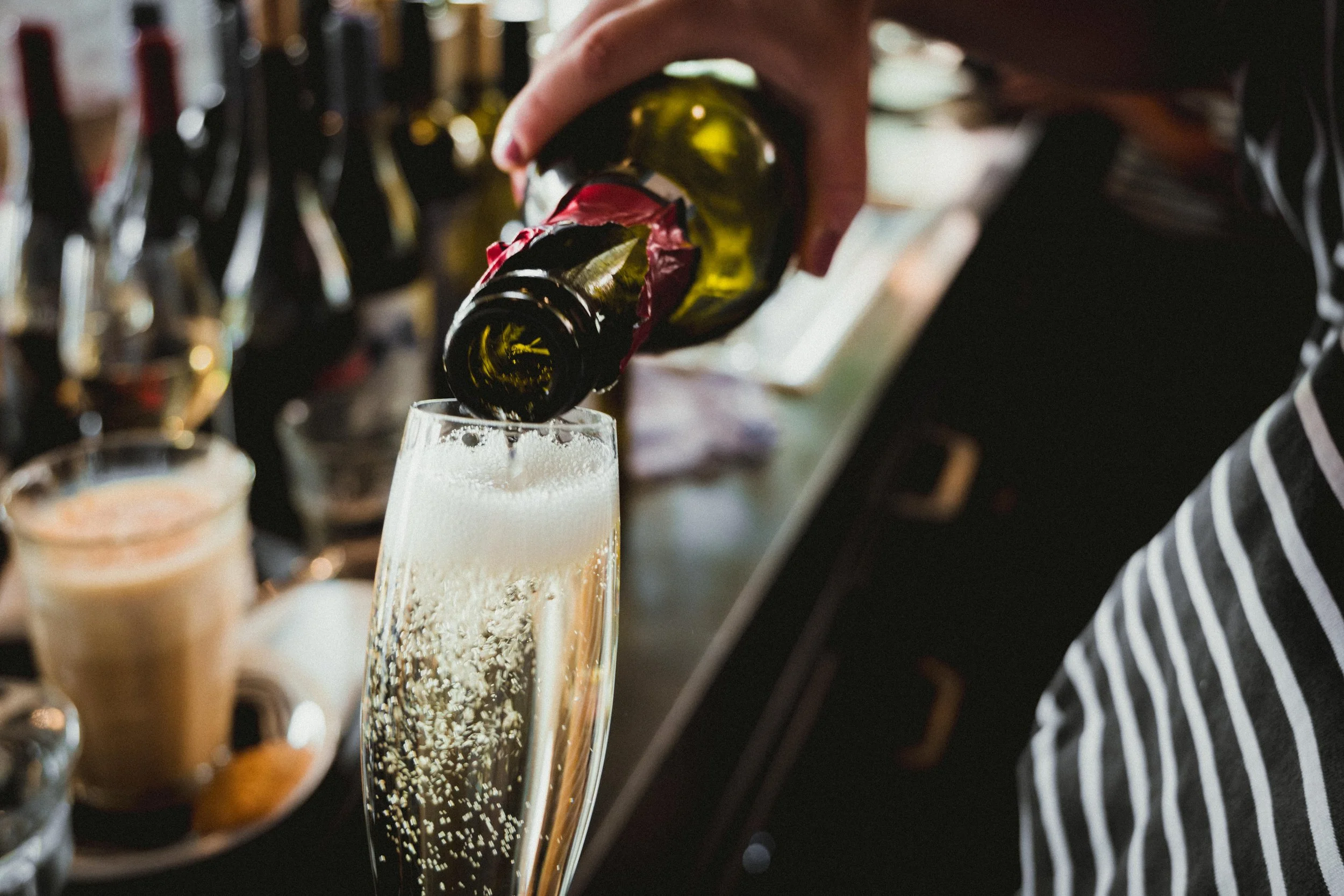 Persoon giet mousserende wijn in een champagneglas op een bar of feestlocatie.