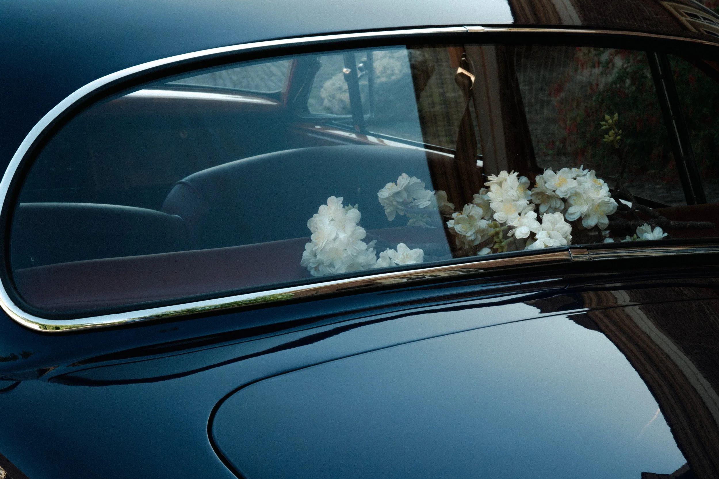 Een zwart veterauto met bloemen op de motorkap, gefotografeerd vanaf de zijkant door de voorruit. trouwauto Ferrari
