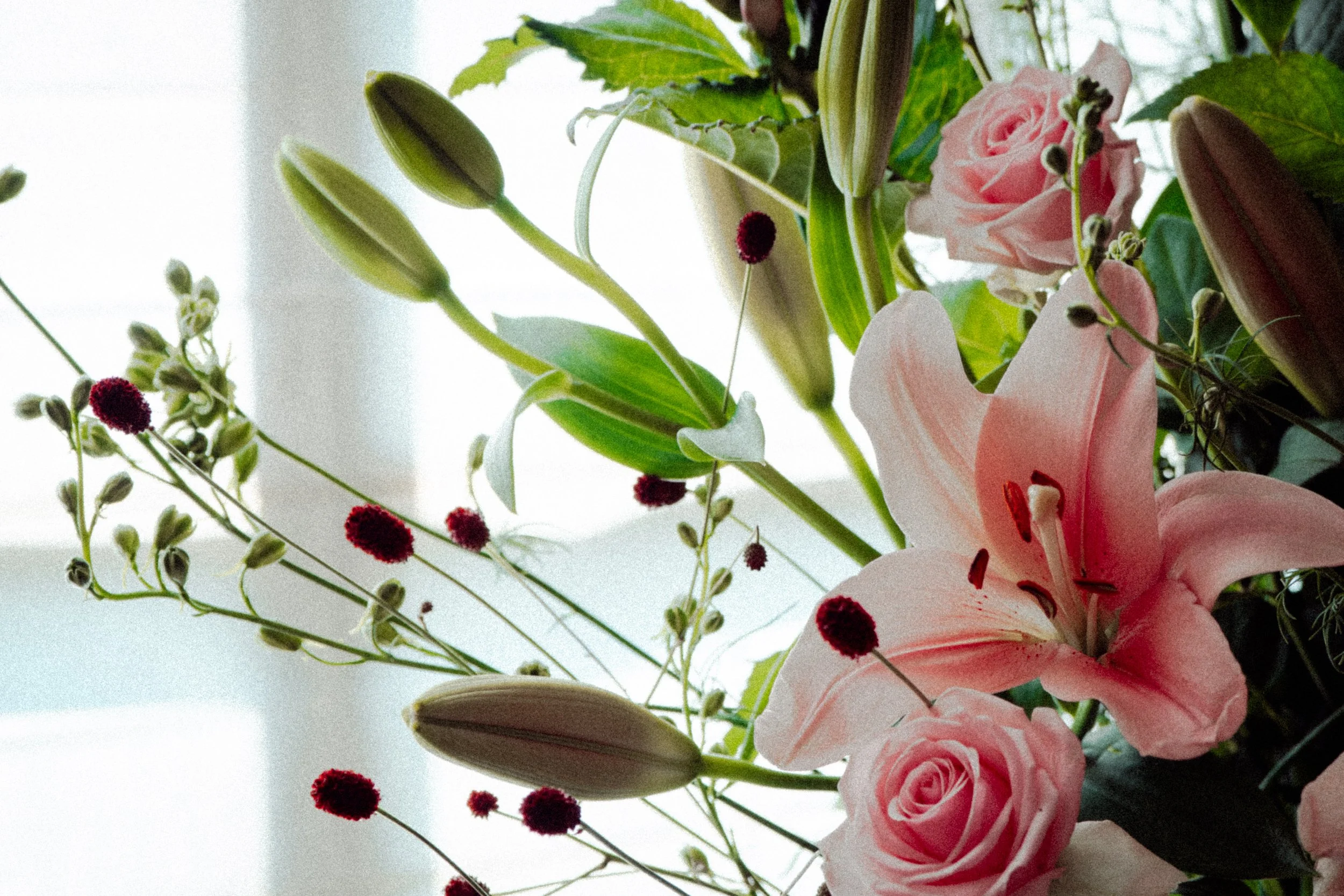 Een boeket bloemen met roze rozen, witte lelies en kleine rode en witte bloemen, gezet in een vaas voor een raam. bruidsboeket bruiloft bruid 
