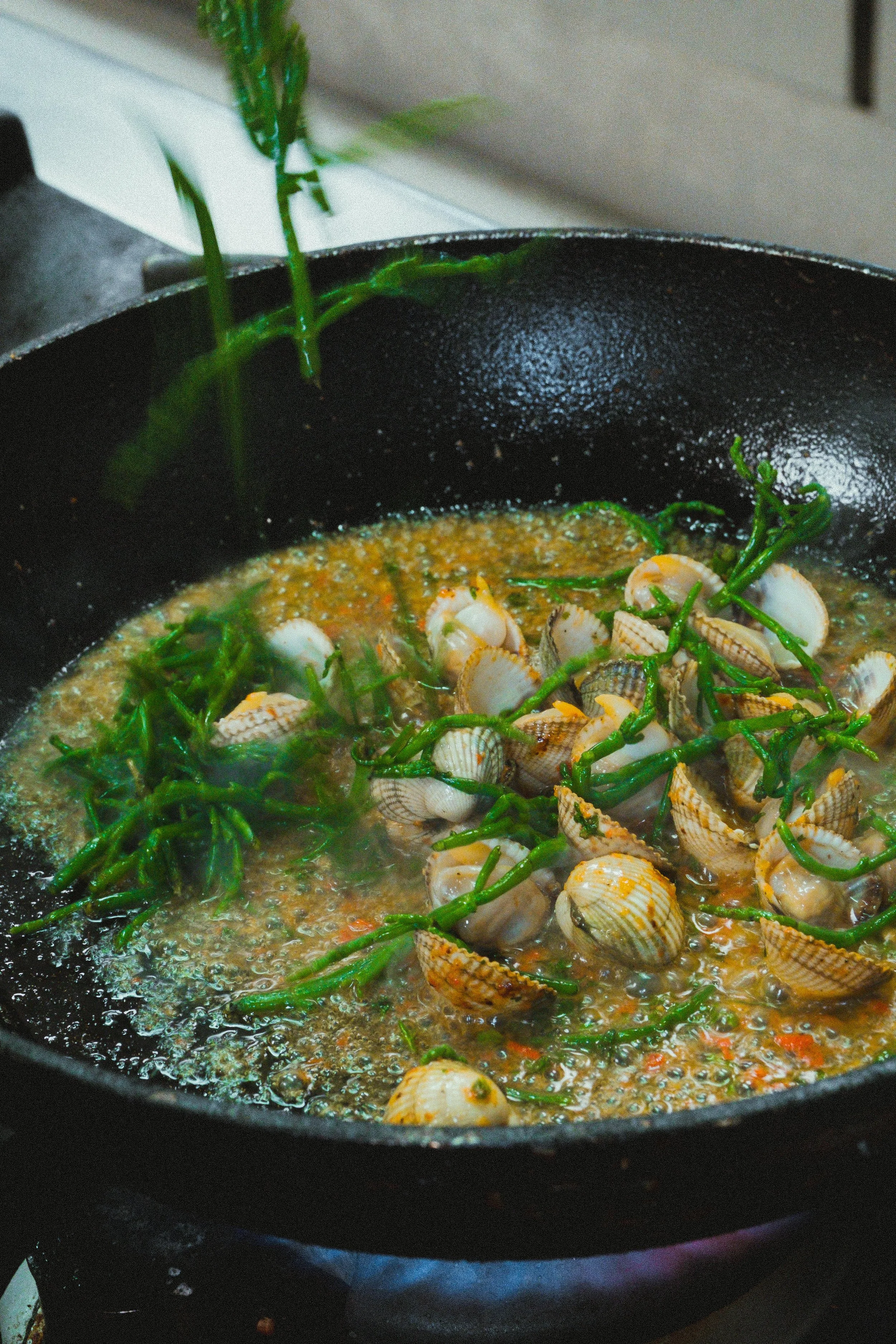 Zeewier, schelpen en een saus in een pan