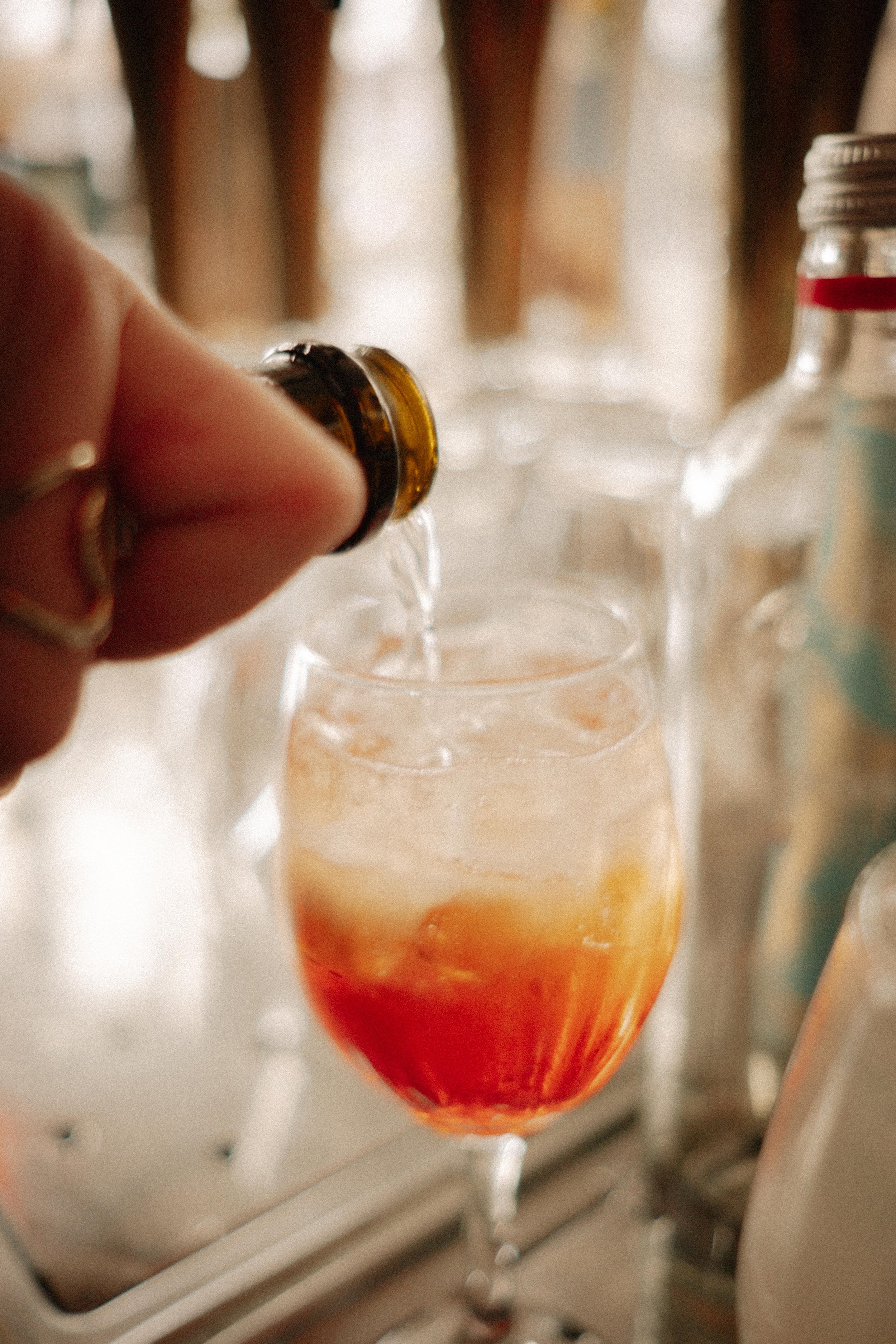 Persoon giet een drankje uit een kleine fles in een glas met een kleurrijke inhoud, op een dienblad met andere glazen.