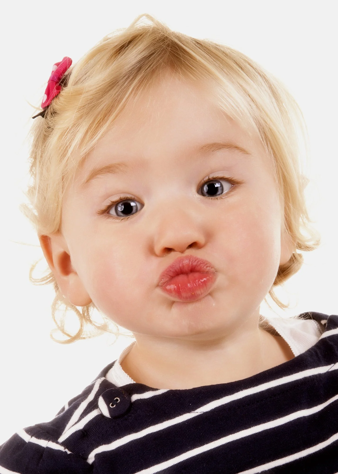 Close-up of a young girl with blonde, curly hair, making a playful pout with her lips, wearing a black and white striped hoodie.