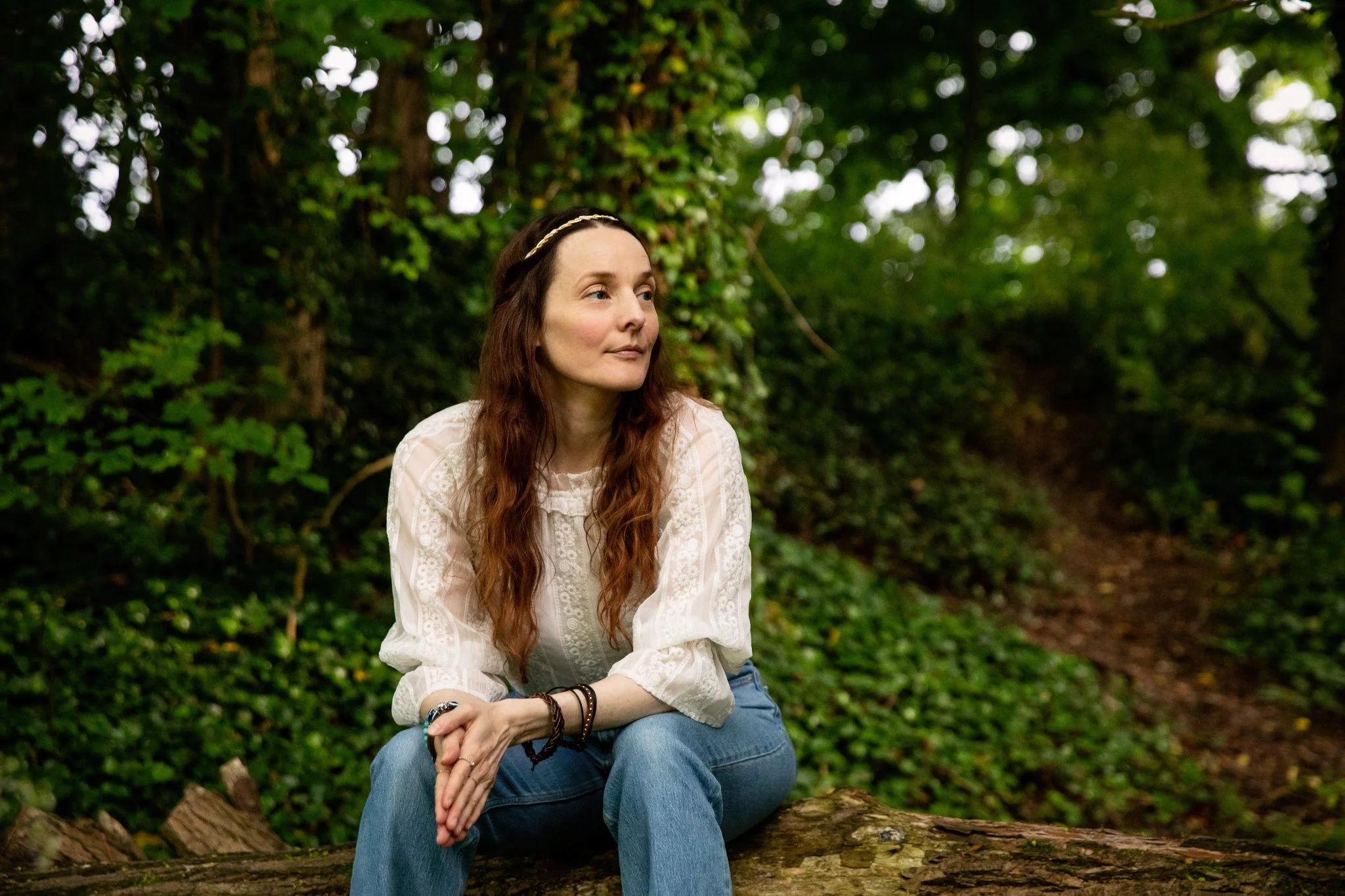 An image of Harmony Healing founder Claire Buttrum sat on a log in the woods near Cambridge