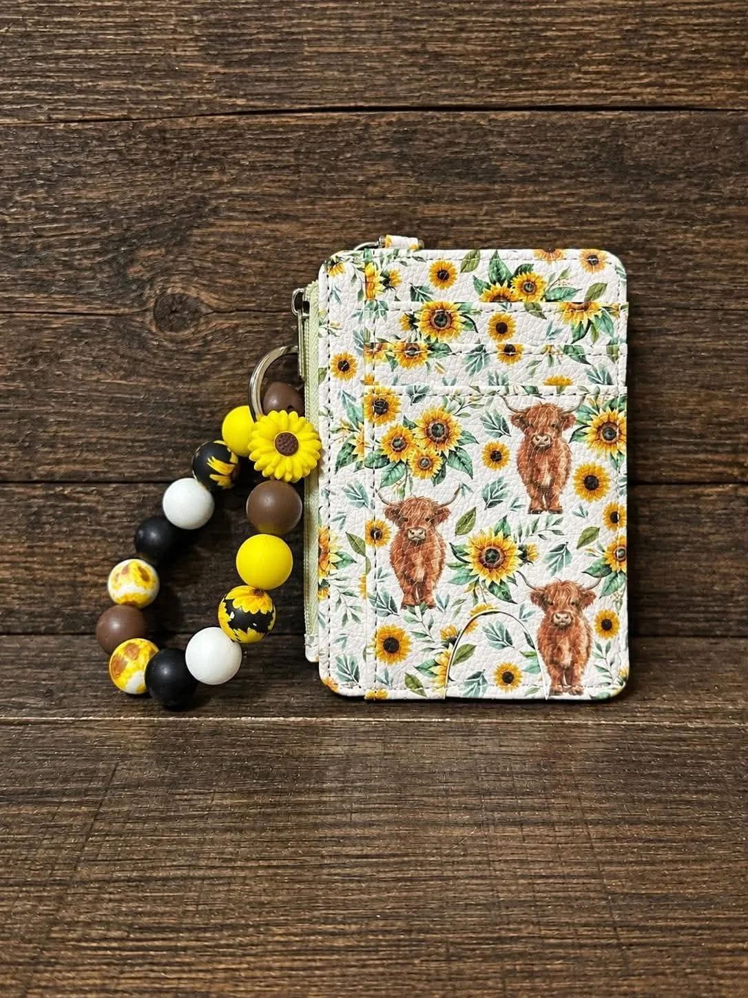 A quilted fabric pouch with sunflower and cow patterns and a sunflower and chicken bead teething necklace on a wooden surface.
