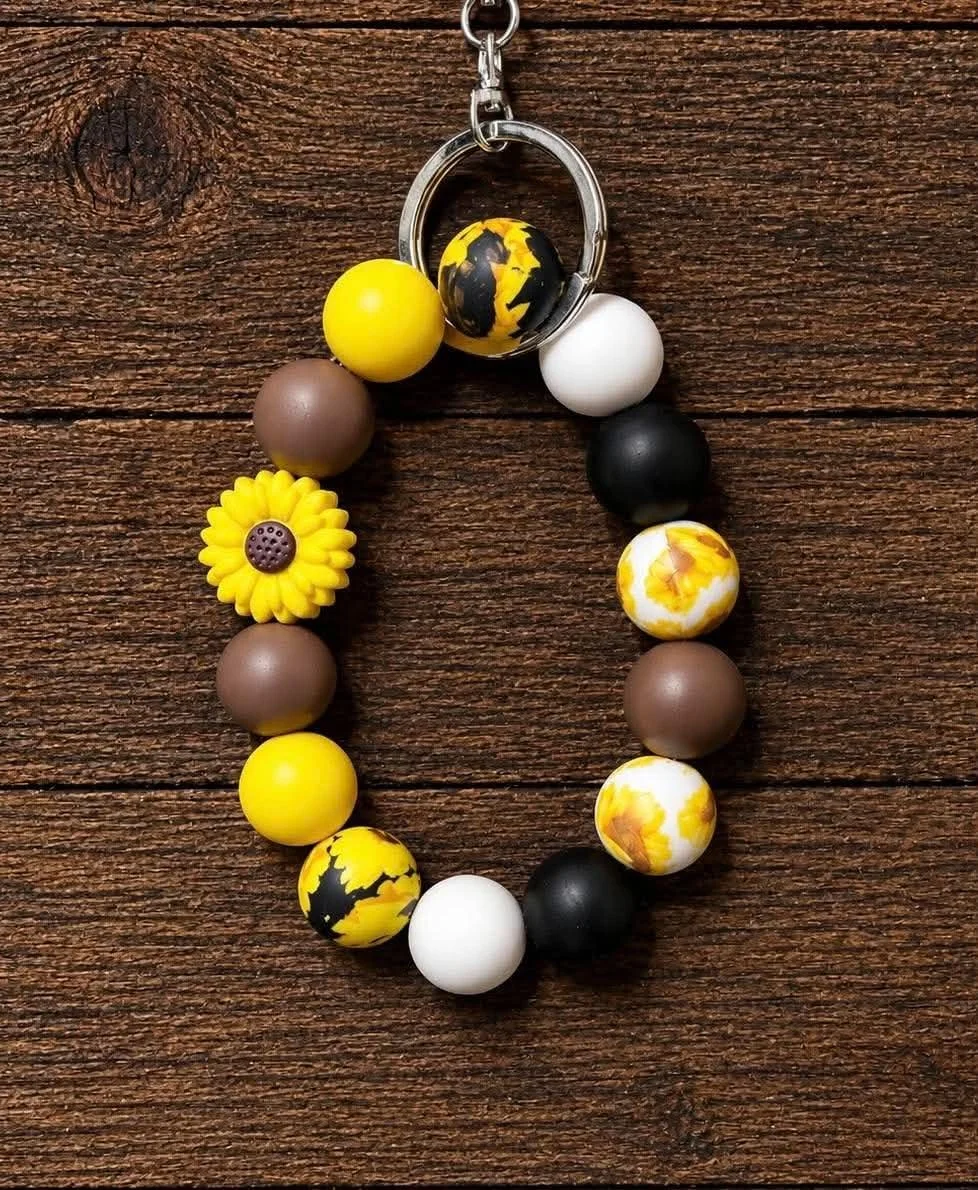 A beaded keychain with round beads in yellow, black, white, and brown, and a yellow flower-shaped bead, on a wooden surface.
