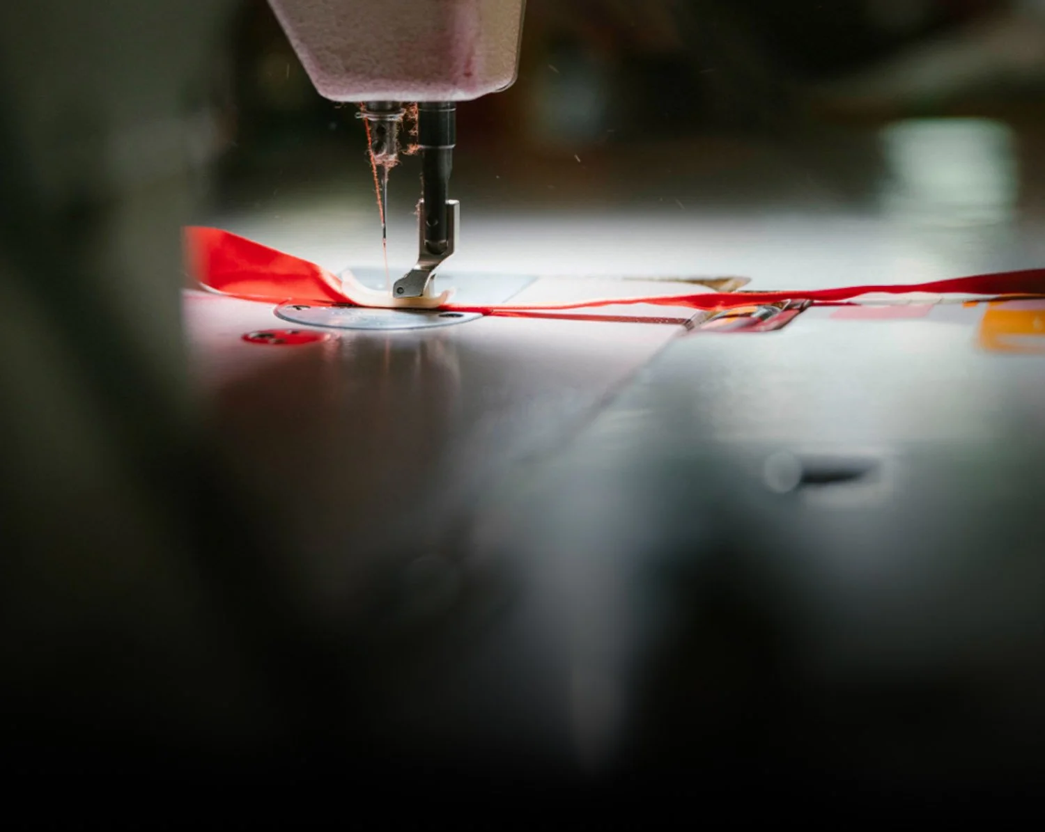 Close-up of machinery sewing red fabric on a sewing machine.