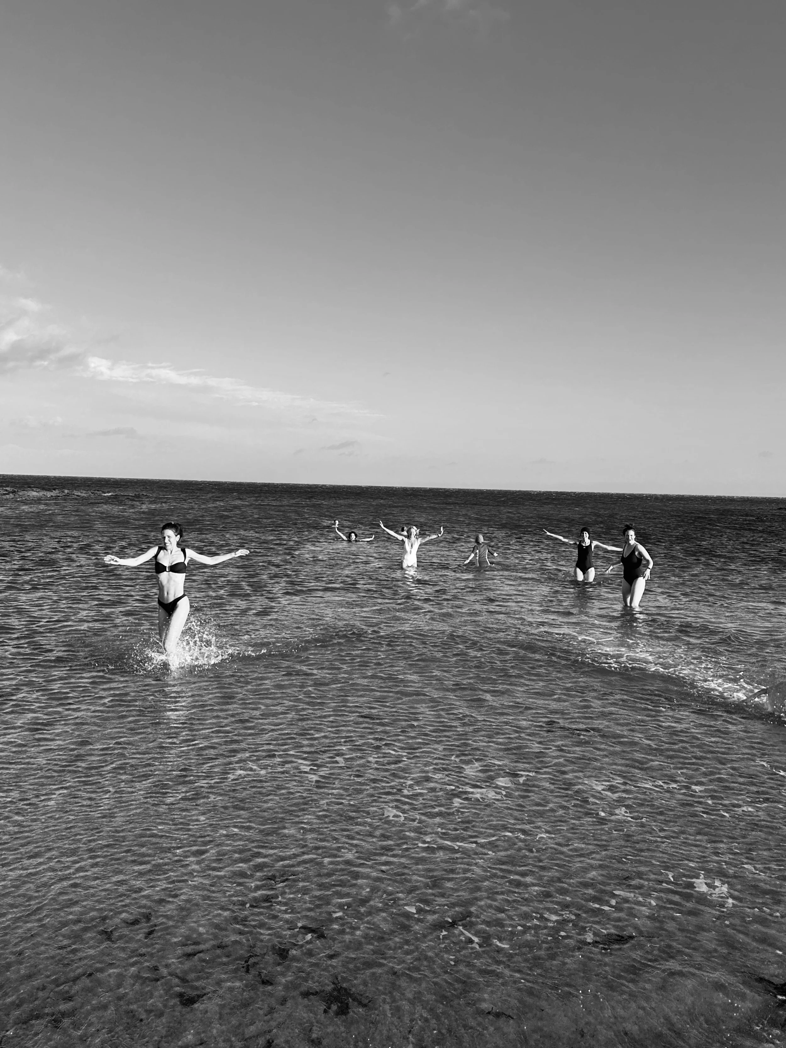 People enjoying swimming and playing in the ocean along the beach with a cloudy sky above.