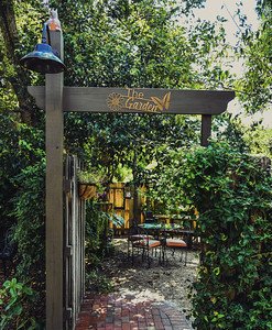 Garden entrance with a sign reading 'The Garden', surrounded by lush greenery and a brick pathway.