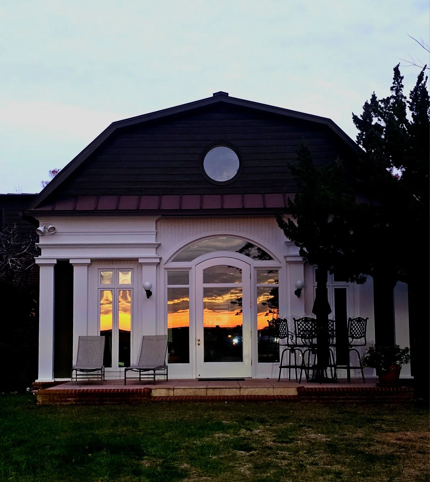 White house patio with glass doors, outdoor chairs and table reflecting a vivid sunset.