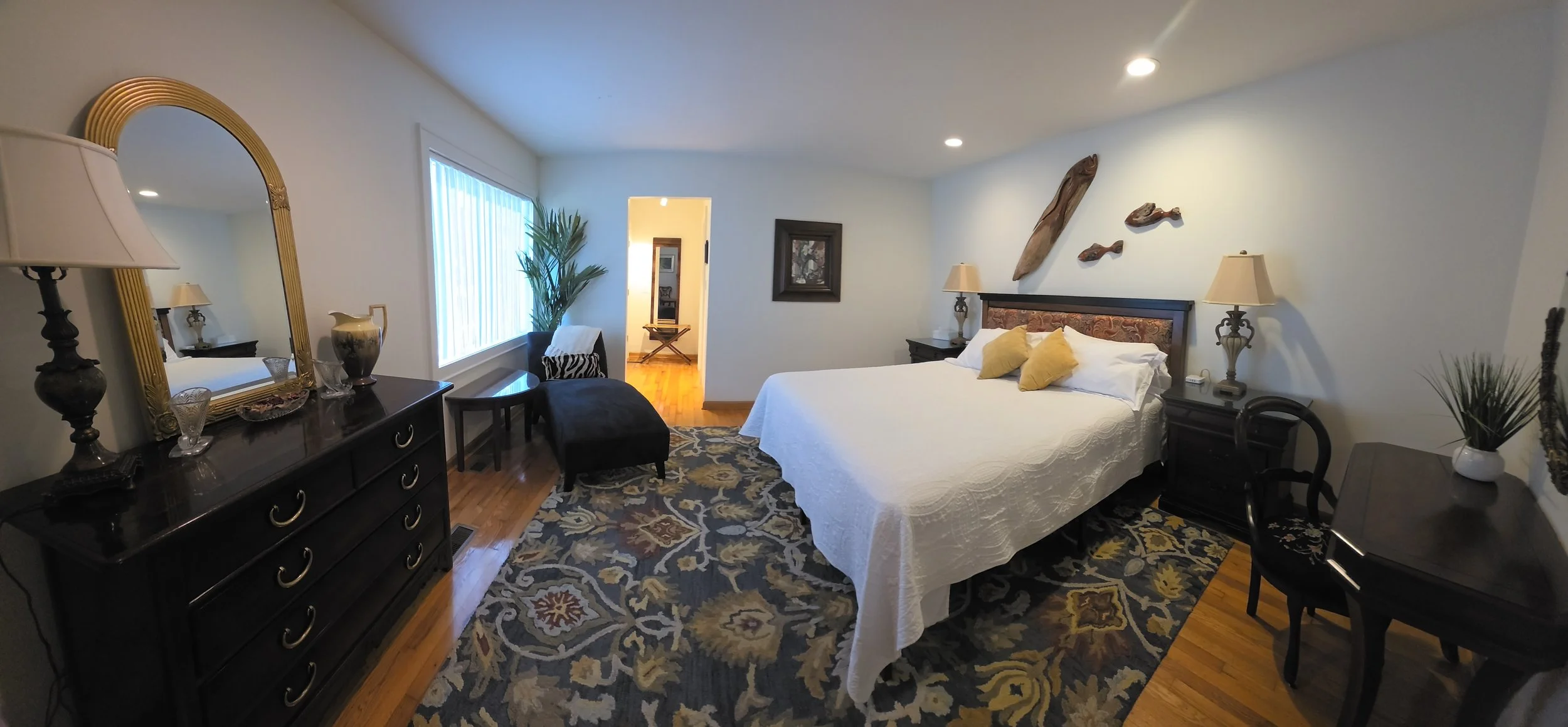 The Marlin Room at Bostwick's Magnolia Manor, featuring a king-size bed with white linens, elegant dark wood furnishings, a gold-framed mirror, and coastal-inspired décor.