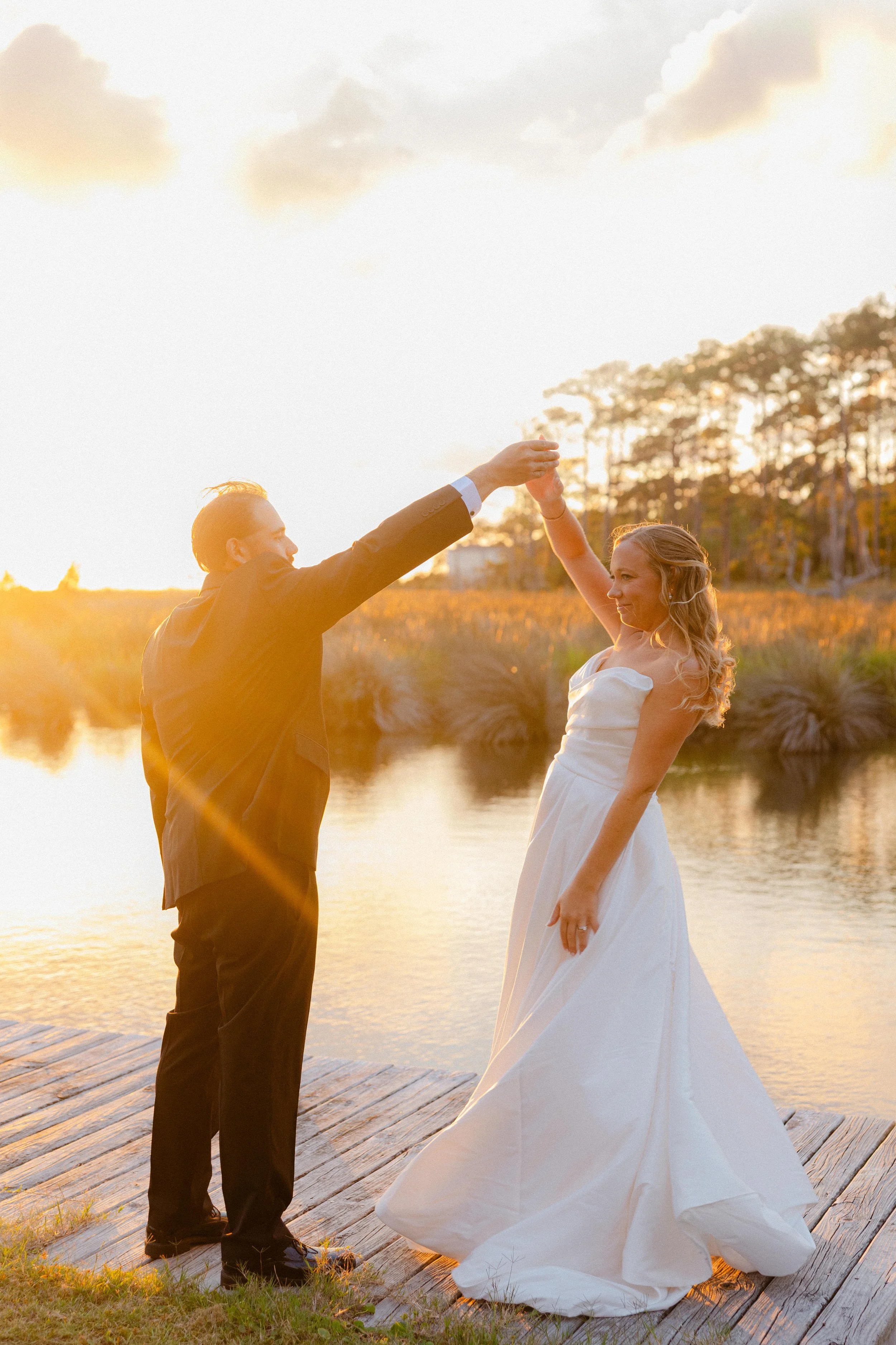 Groom twirling his bride on the wooden dock at Bostwick’s Magnolia Manor, with golden sunset light over the water and marsh.