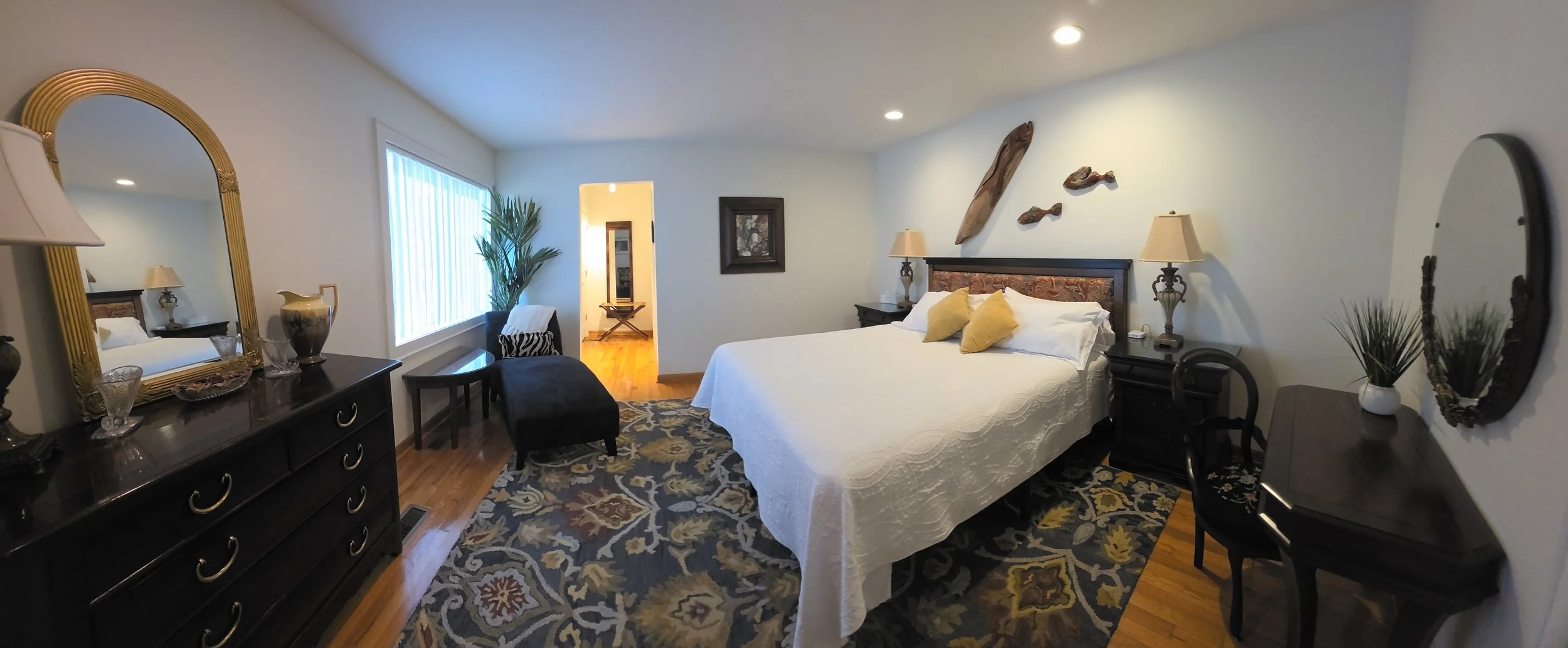 Elegant bedroom with a white bed, yellow accent pillows, dark wood furniture, patterned area rug, and fish-themed wall decor.