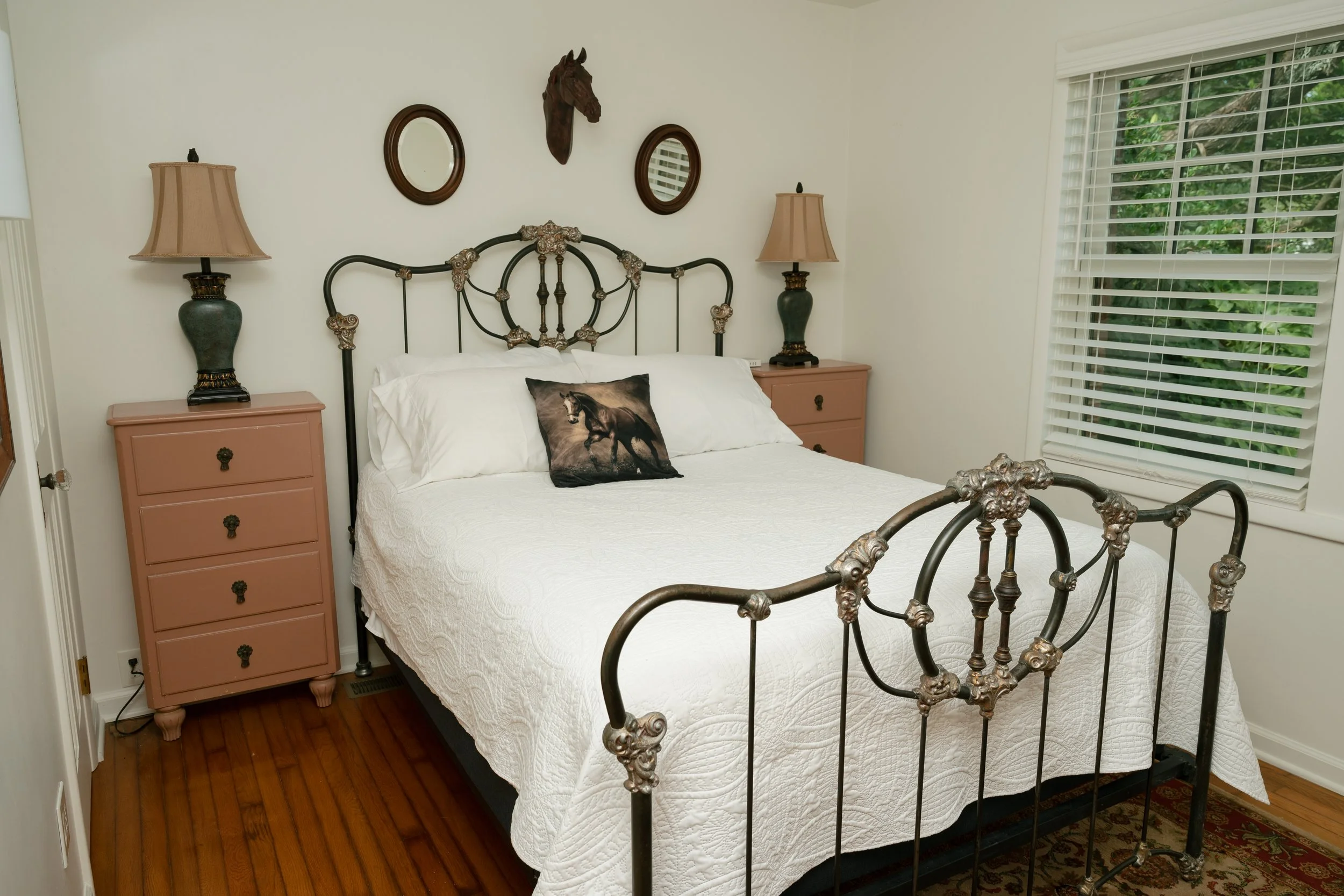 Elegant bedroom with an ornate black metal bed, white quilt, horse-print pillow, matching lamps, dressers, and horse wall decor