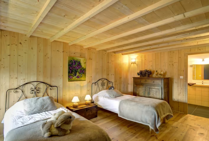 Chambre avec deux lits à baldaquin en fer forgé, décoration en bois, peinture de fleurs sur le mur, deux lampes de chevet allumées, meuble ancien, en ouvrant sur une petite cuisine.