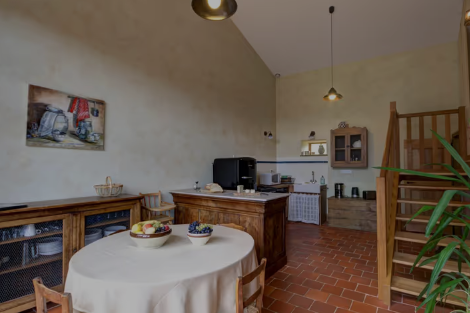 Cuisine rustique avec une table ronde couverte d'une nappe blanche, un grillage en bois, et une étagère murale.