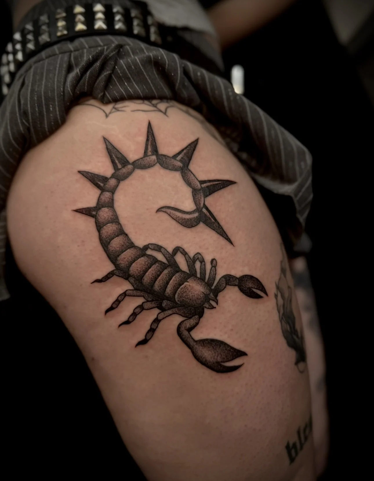 Tattoo of a scorpion with the tail ending in a compass rose on a person's upper arm.