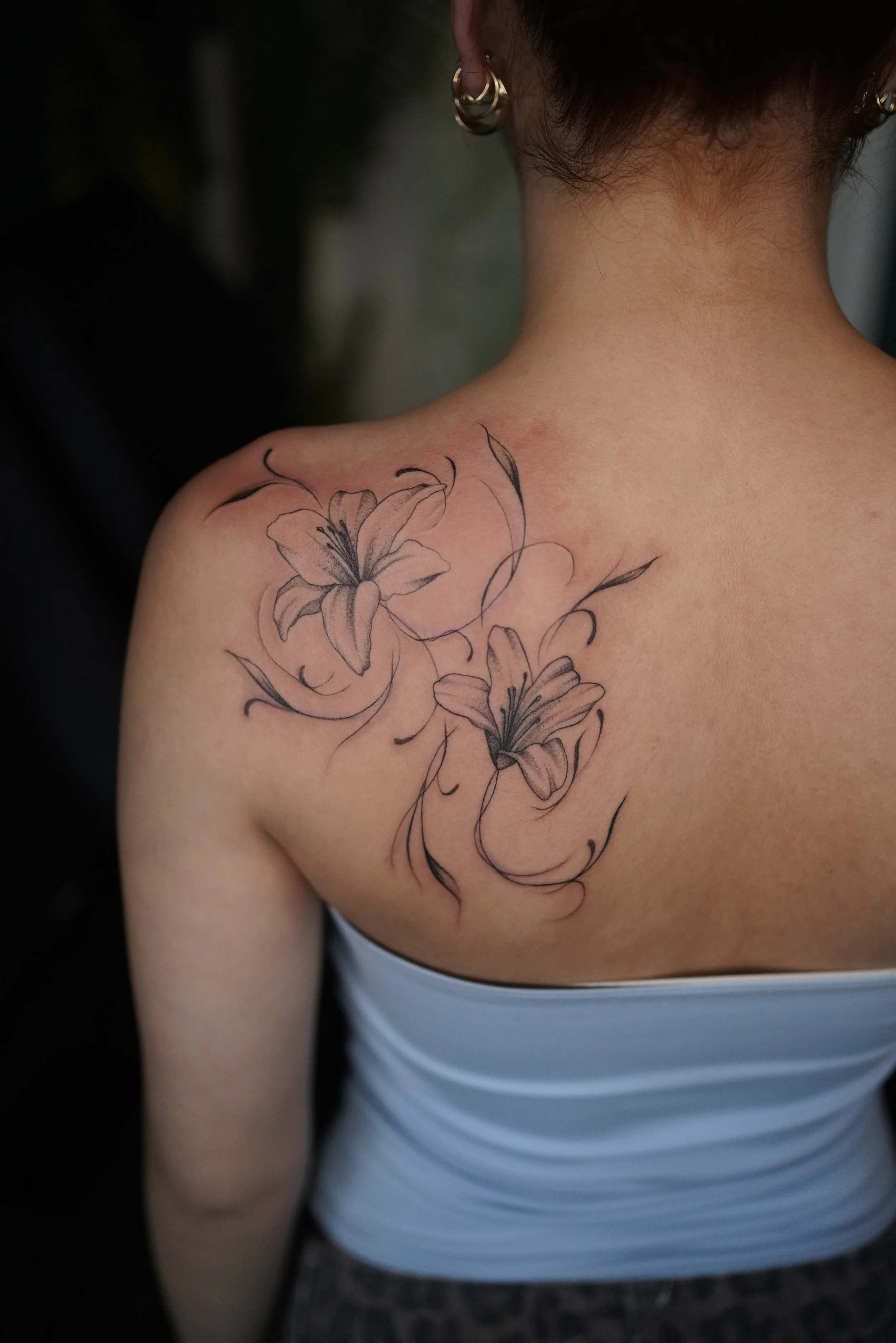 Close-up of a person's back and shoulder with a tattoo of lilies and swirling lines.