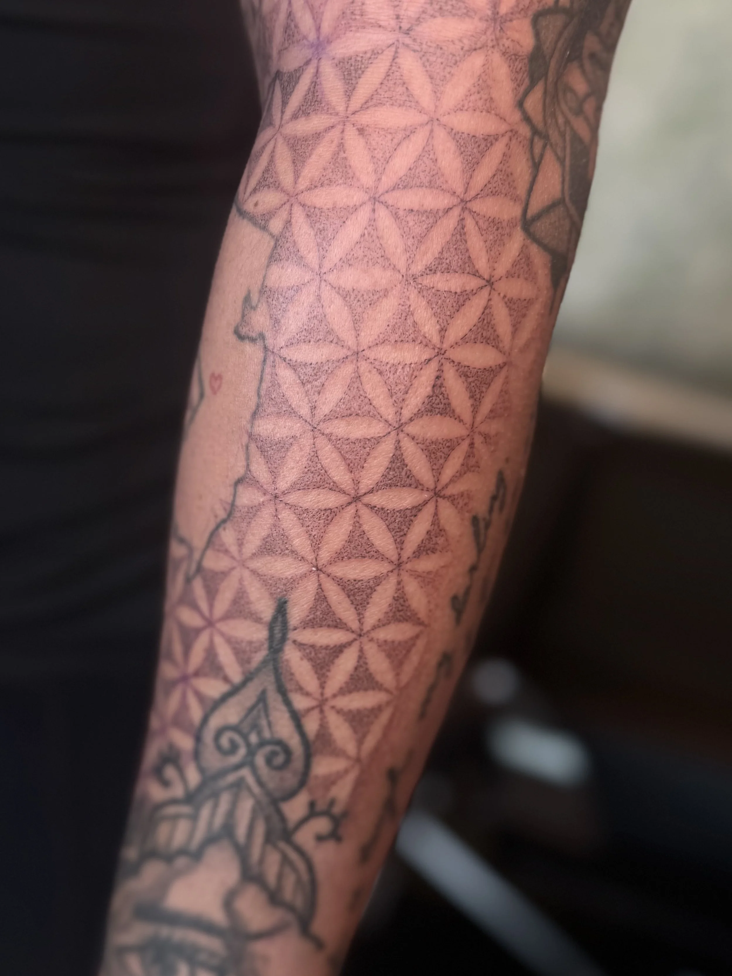 Close-up of a person's arm with a geometric tattoo pattern and additional tattoo elements visible.