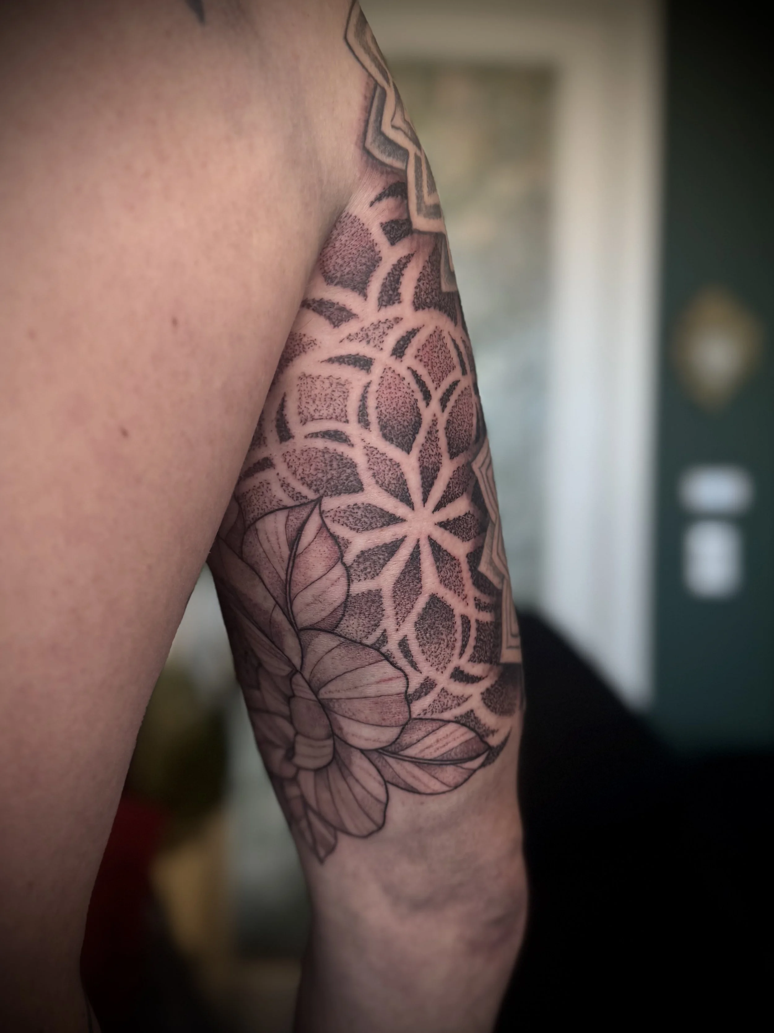 Close-up of a person's arm with a detailed black and gray tattoo featuring a floral and geometric design.