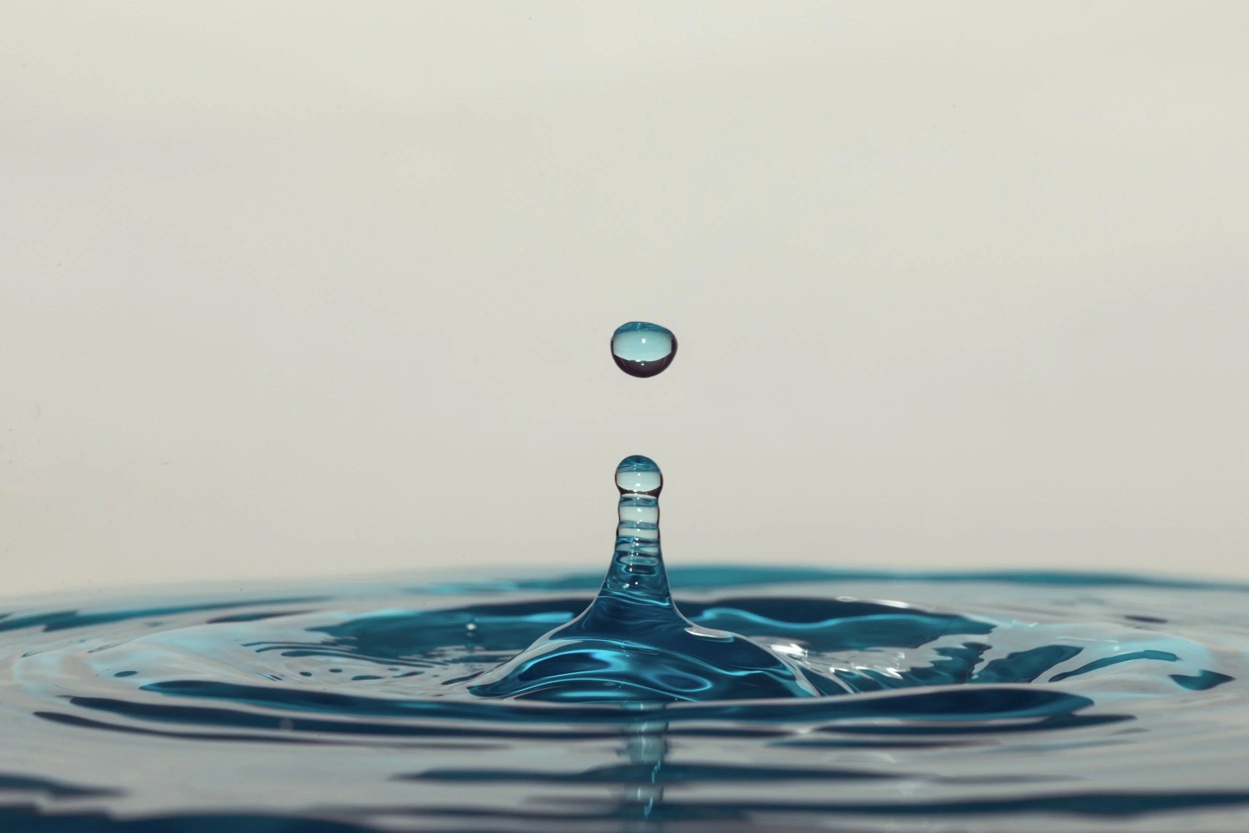 Close-up of a water droplet falling into a calm water surface, creating ripples.