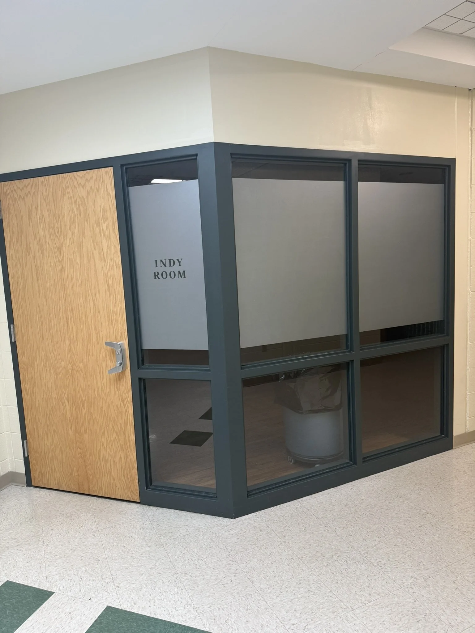 An educational or office space with a door labeled 'Indy Room', glass windows, and a trash can inside.