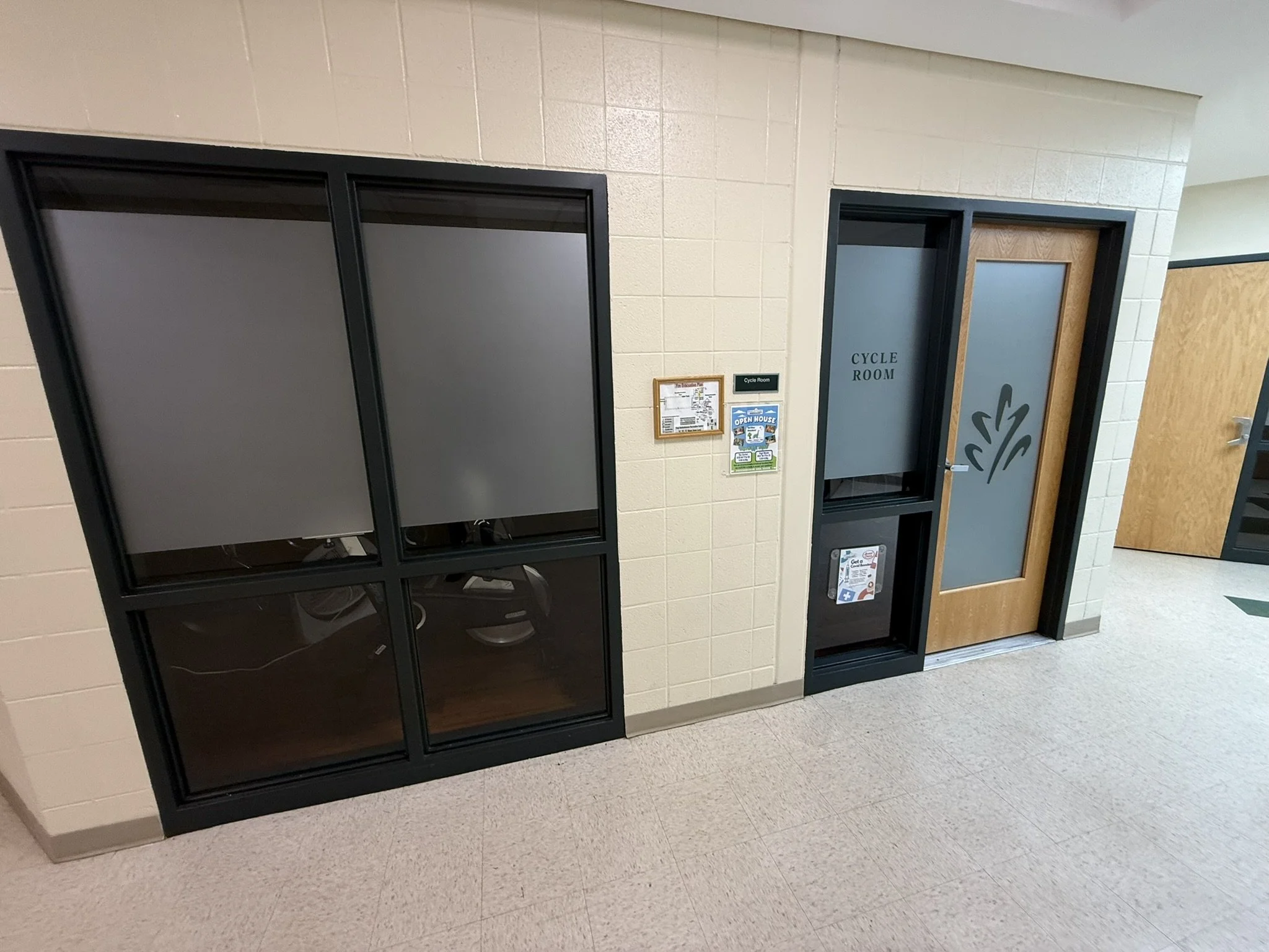 Two black lockers in a school hallway, one with frosted glass doors and the other with wooden doors, near a door labeled 'Cycle Room'.