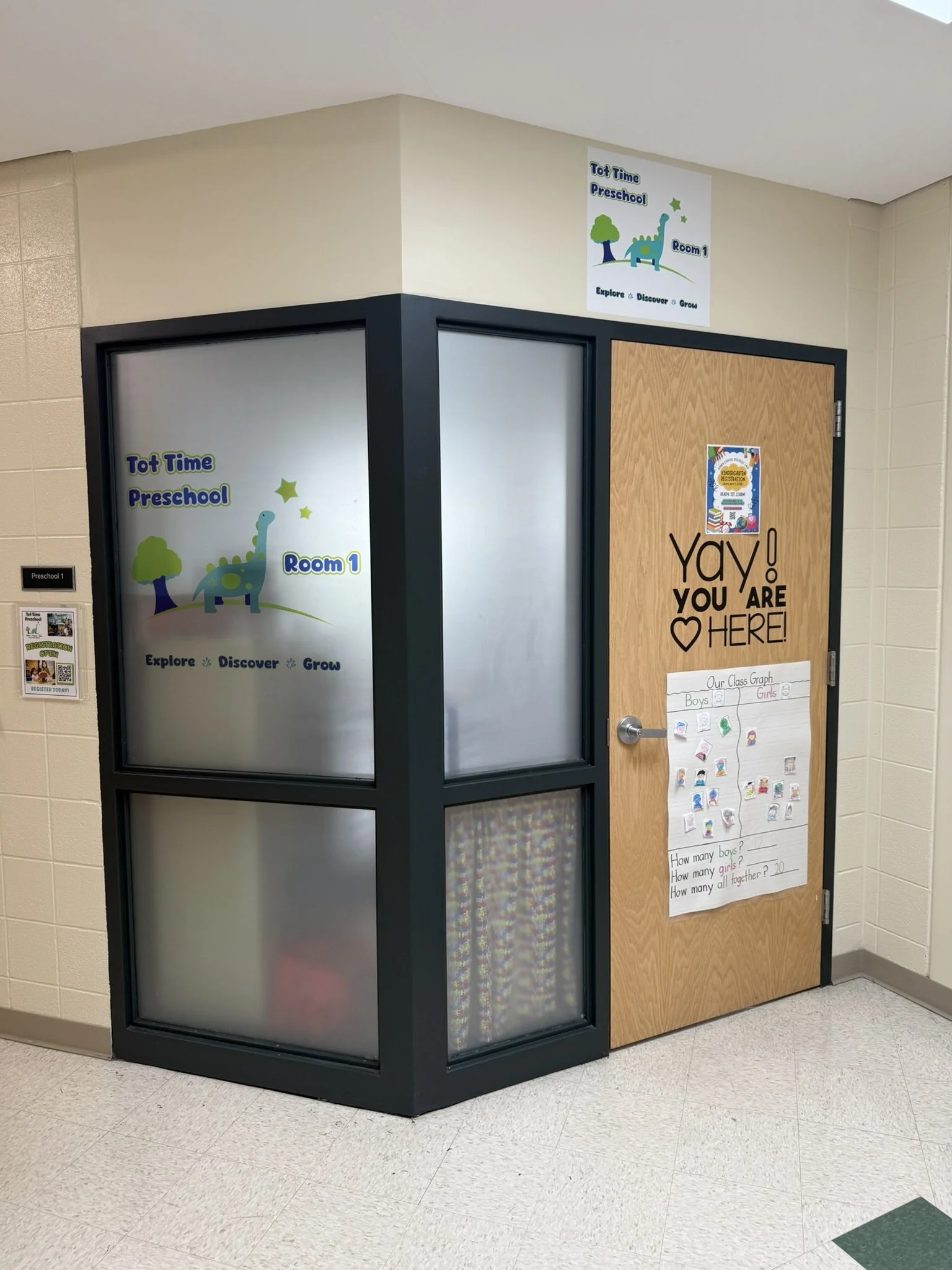 School hallway corner with a doorway labeled 'Preschool 1' and educational posters about preschool age group, class graph, and a celebration message on the door.
