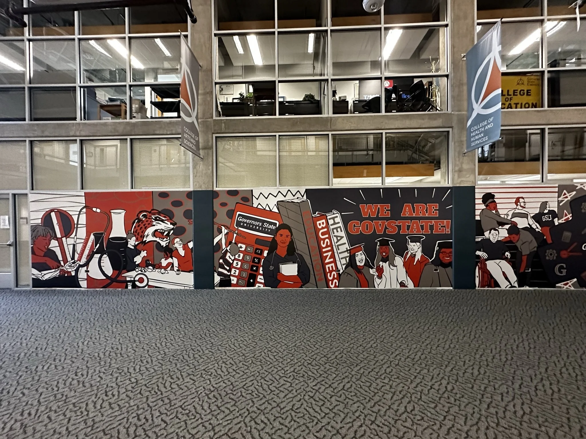 A large window display with a mural showing students, a lion mascot, scientific equipment, and graduation caps, celebrating college students and education.