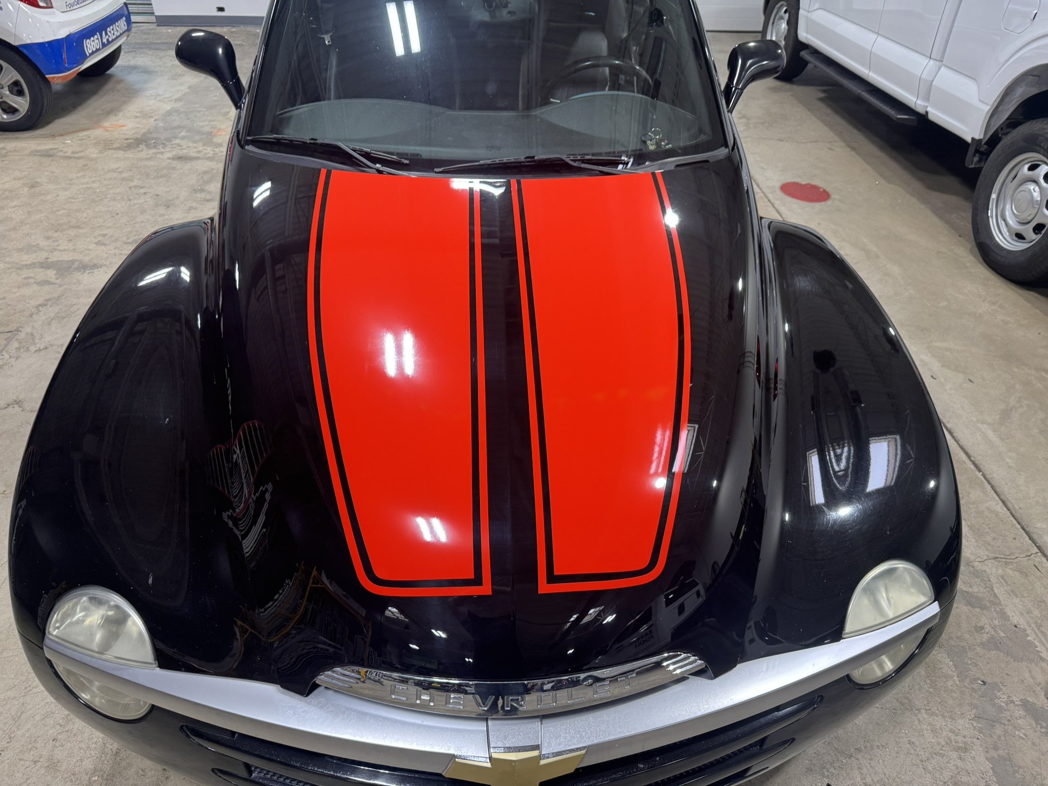 Black Chevrolet car with red racing stripes on the hood, parked in an indoor garage.